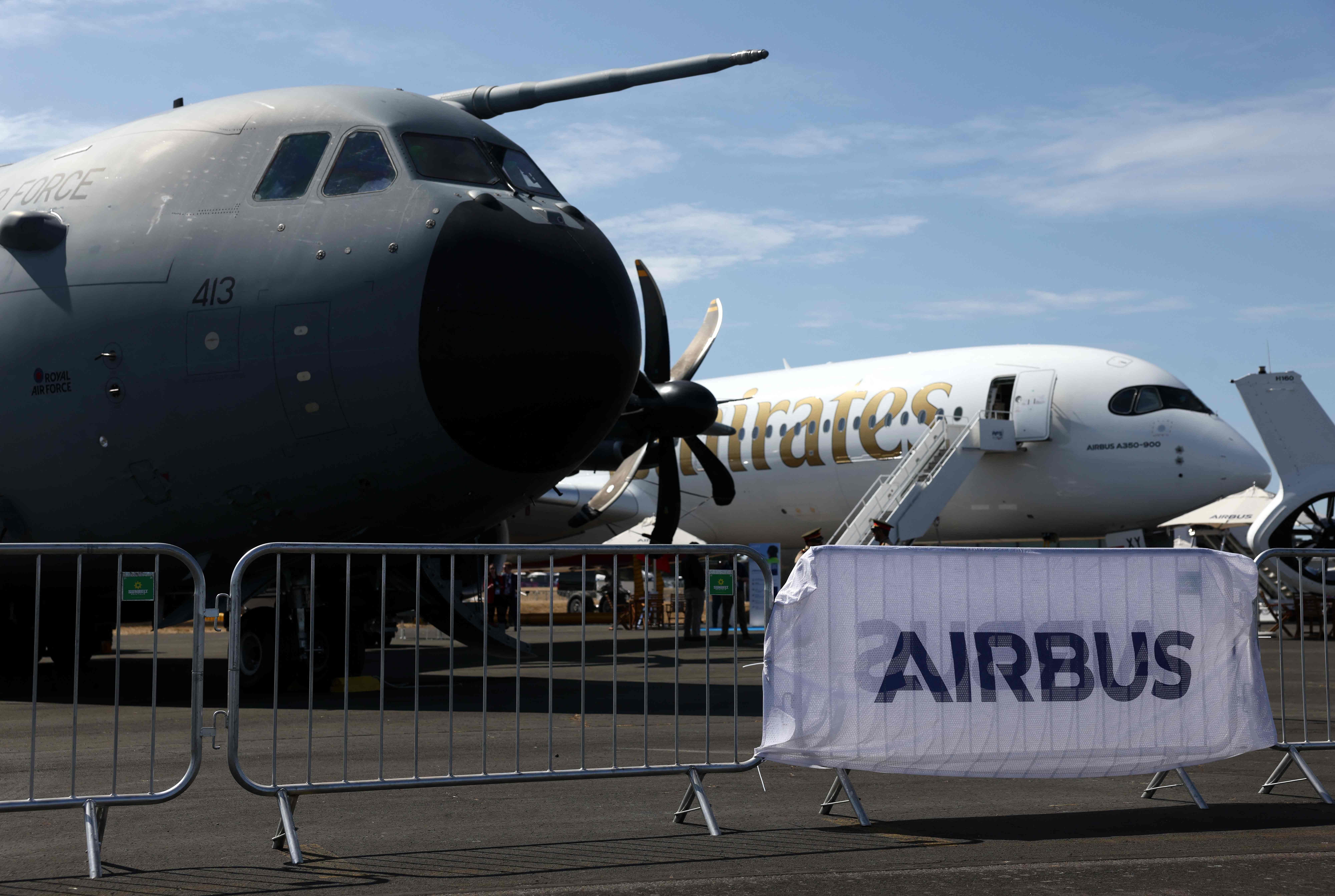 Zwei Flugzeuge nahe einem Airbus-Logo bei einer Luftfahrtausstellung unter blauem Himmel.