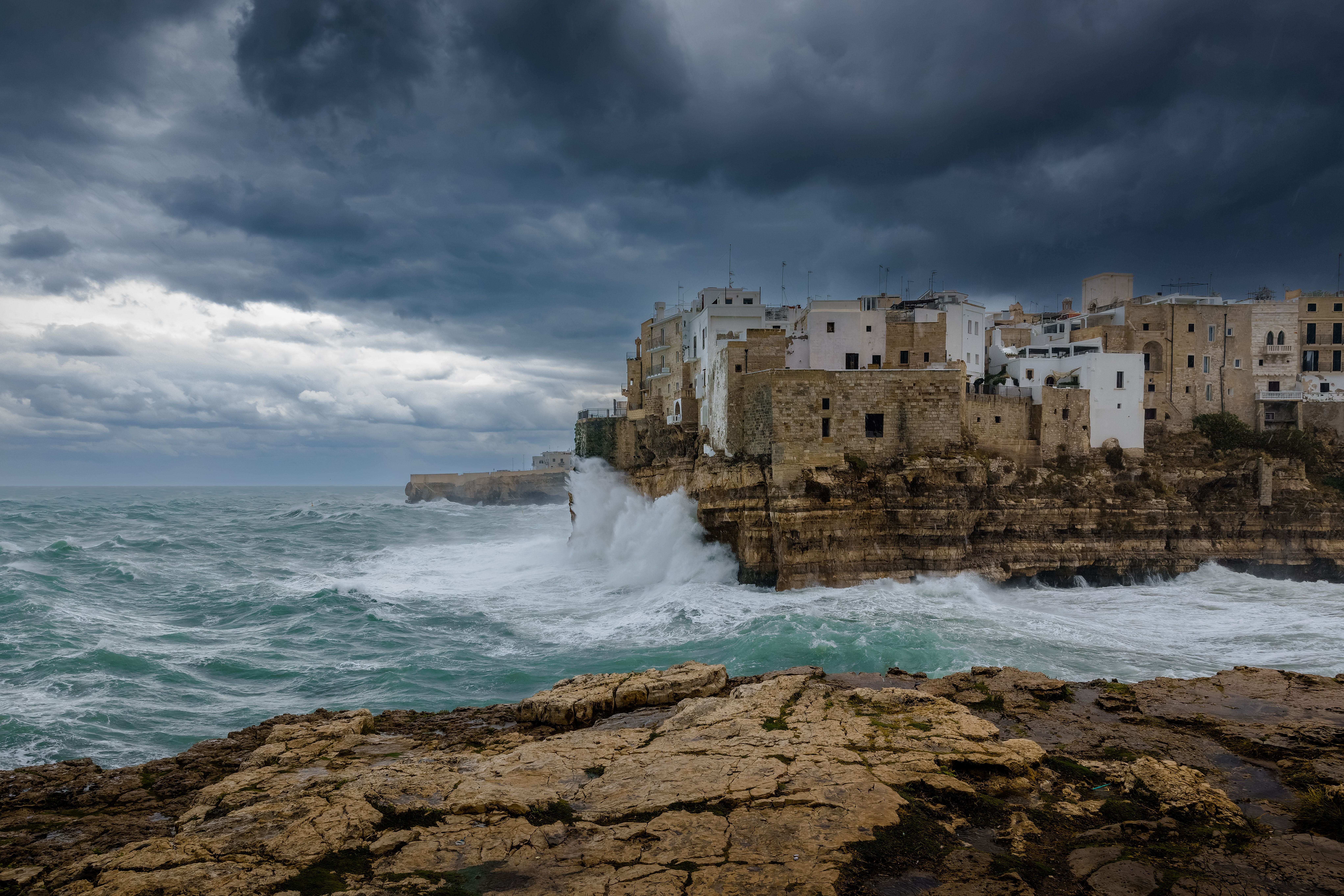 Stürmische Wellen schlagen an die Felsen und Häuser von Polignano a Mare unter dunklen Wolken.