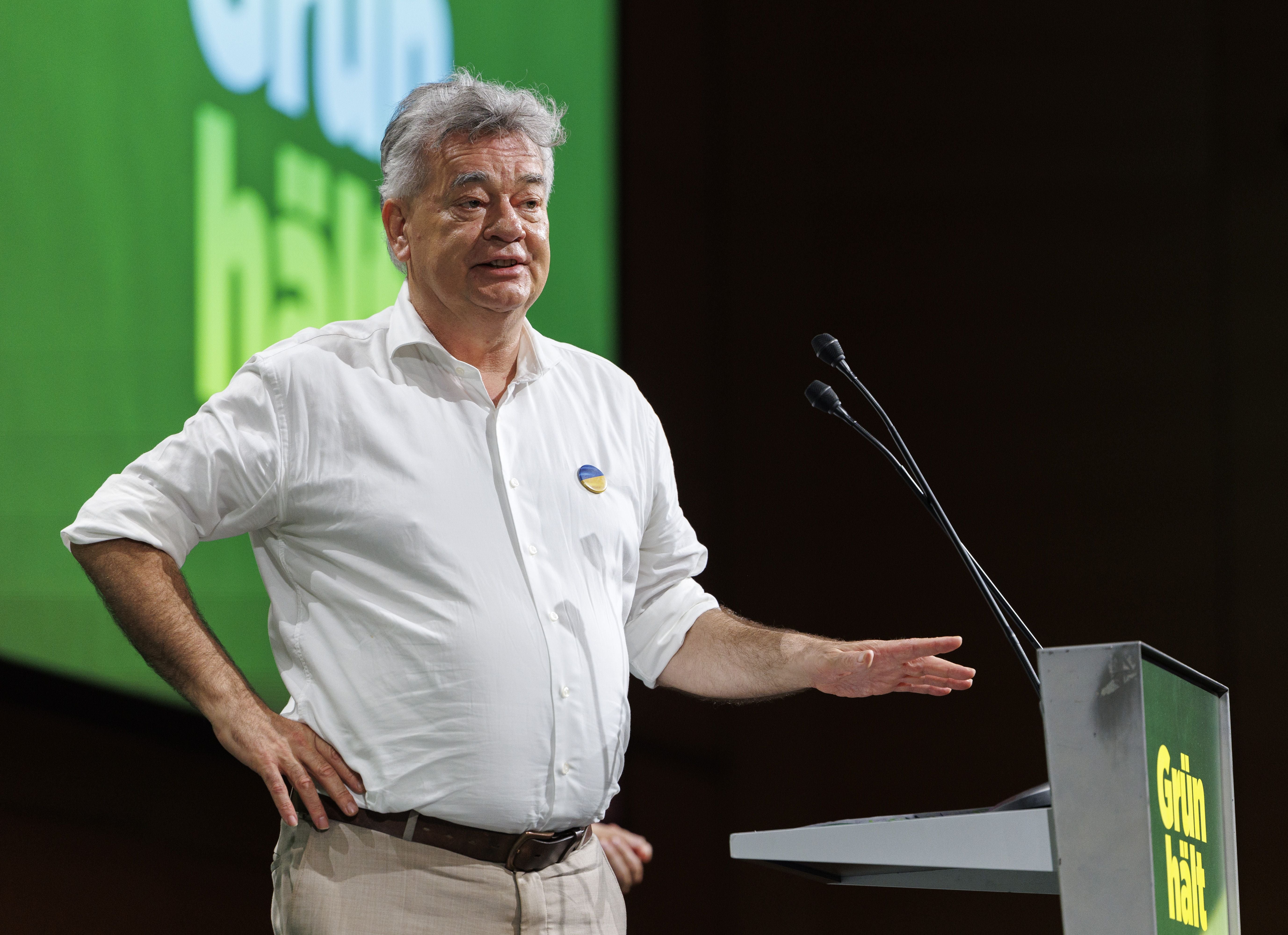 Mann spricht bei einem Kongress am Rednerpult mit grünem "Grün hält"-Schild.