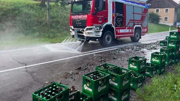 Feuerwehrauto reinigt Straße nach Unfall mit zerbrochenen Bierkästen und Flaschen.