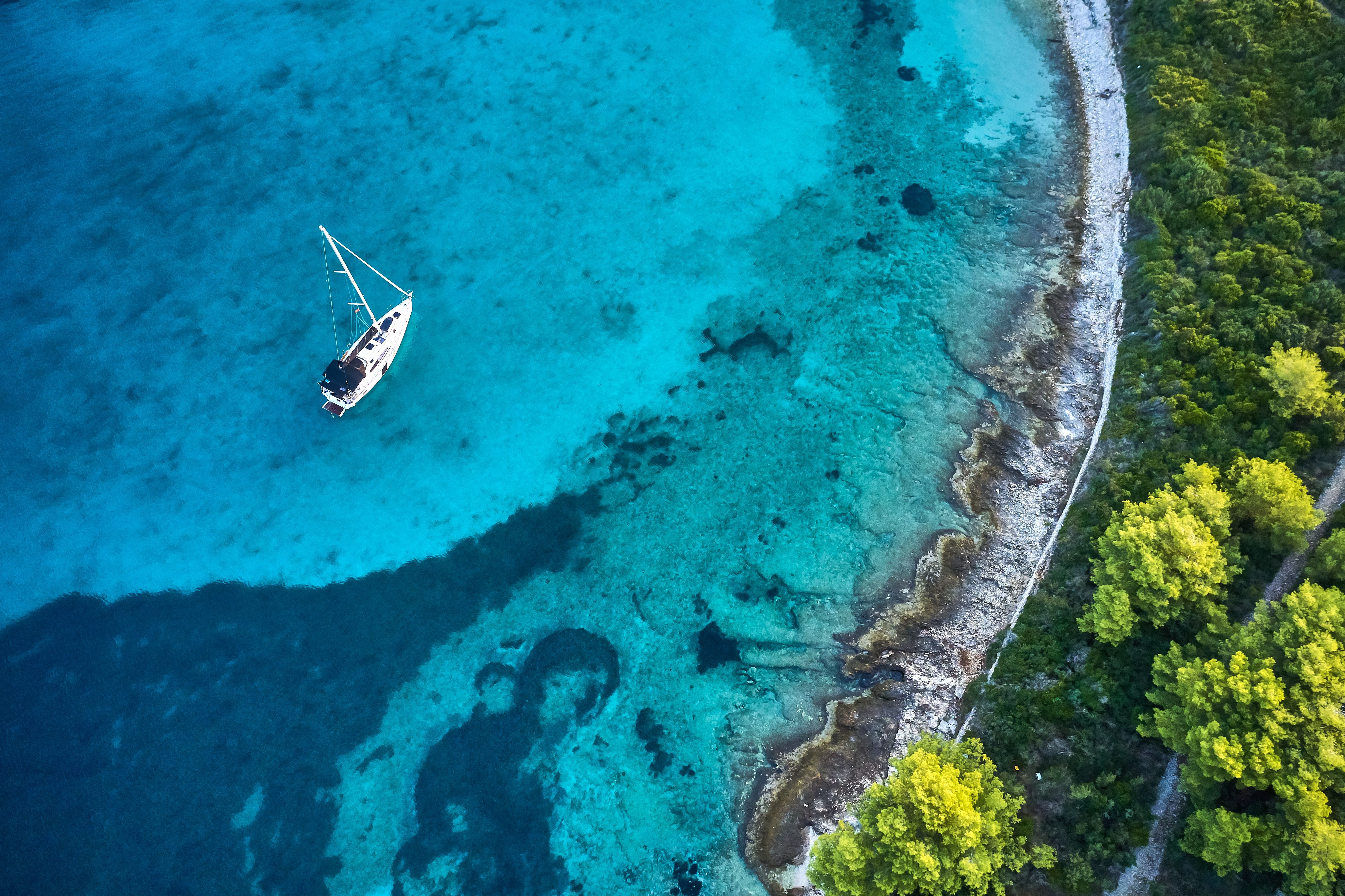 Segelboot ankert im klaren, türkisblauen Meer nahe einer bewaldeten Küste in Dalmatien, Kroatien.