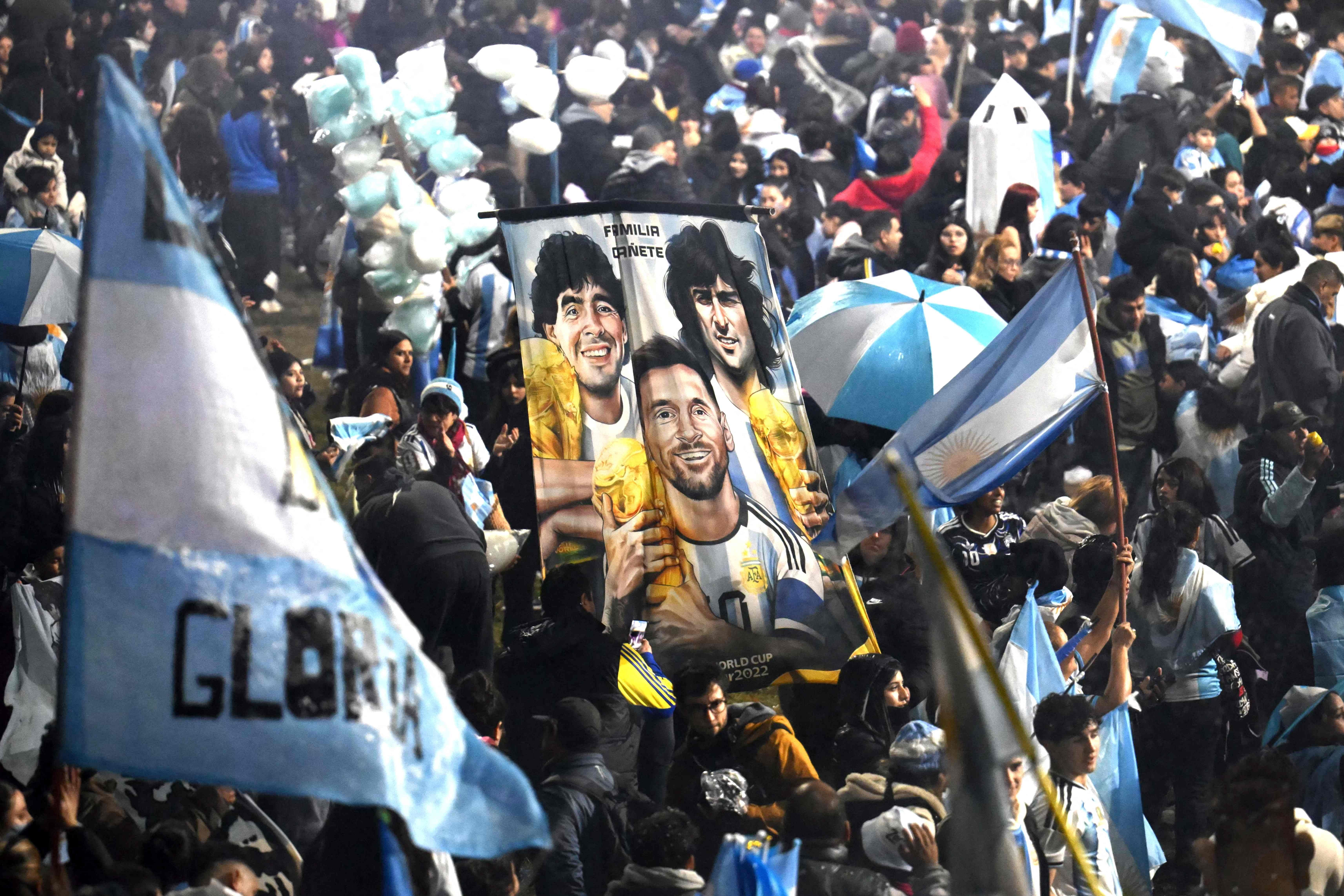 Argentinische Fans halten ein Banner mit Maradona, Kempes und Messi bei einer Menschenmenge mit Flaggen.