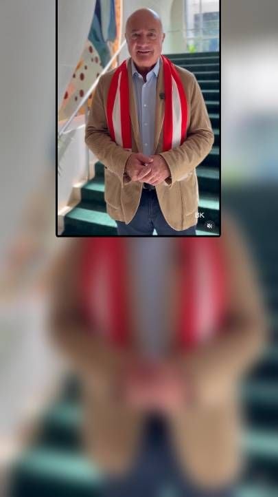 Ein Mann im Sakko mit rot-weißem Schal steht auf einer Treppe und blickt in die Kamera.