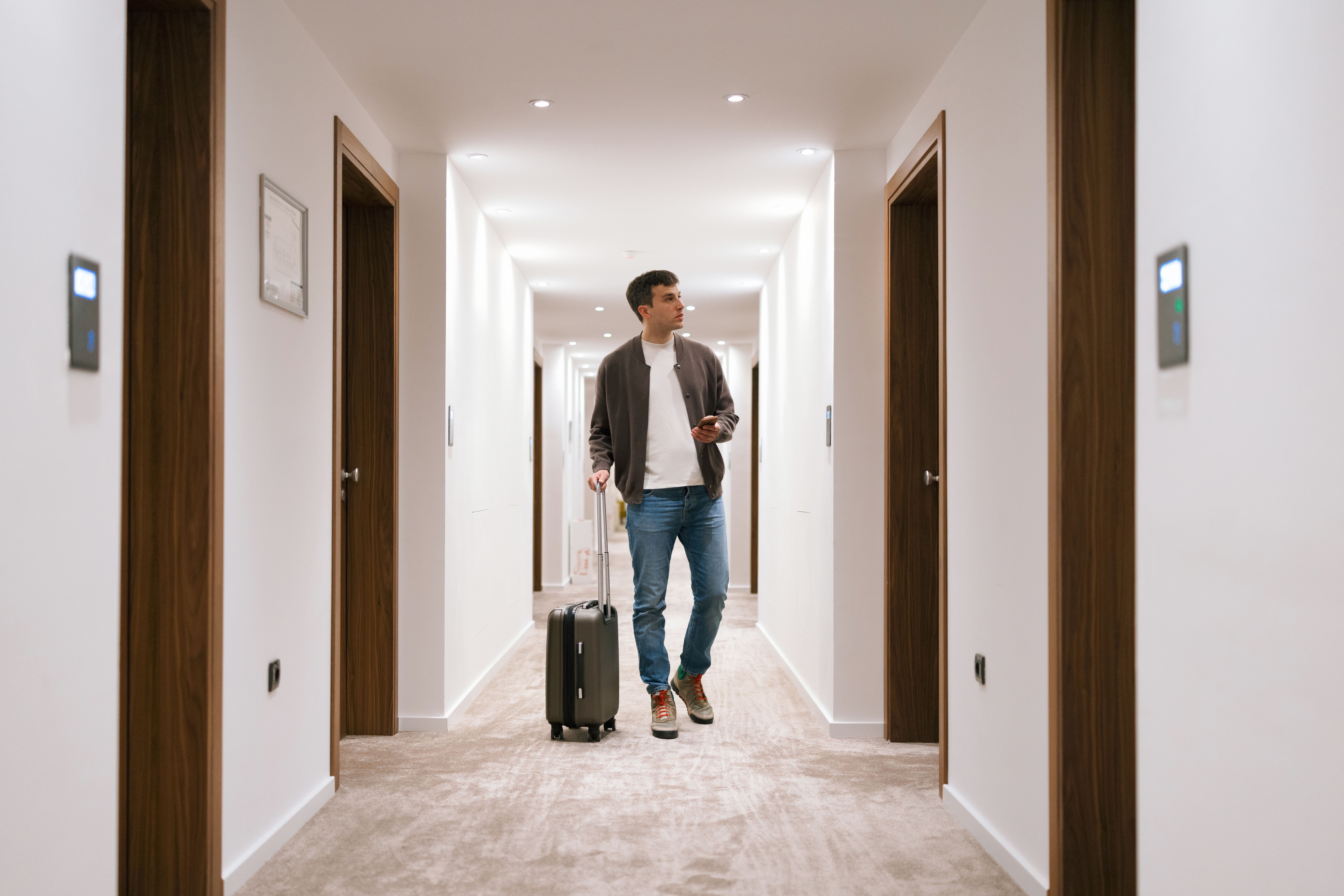 Mann mit Rollkoffer läuft durch einen hellen Hotelflur.