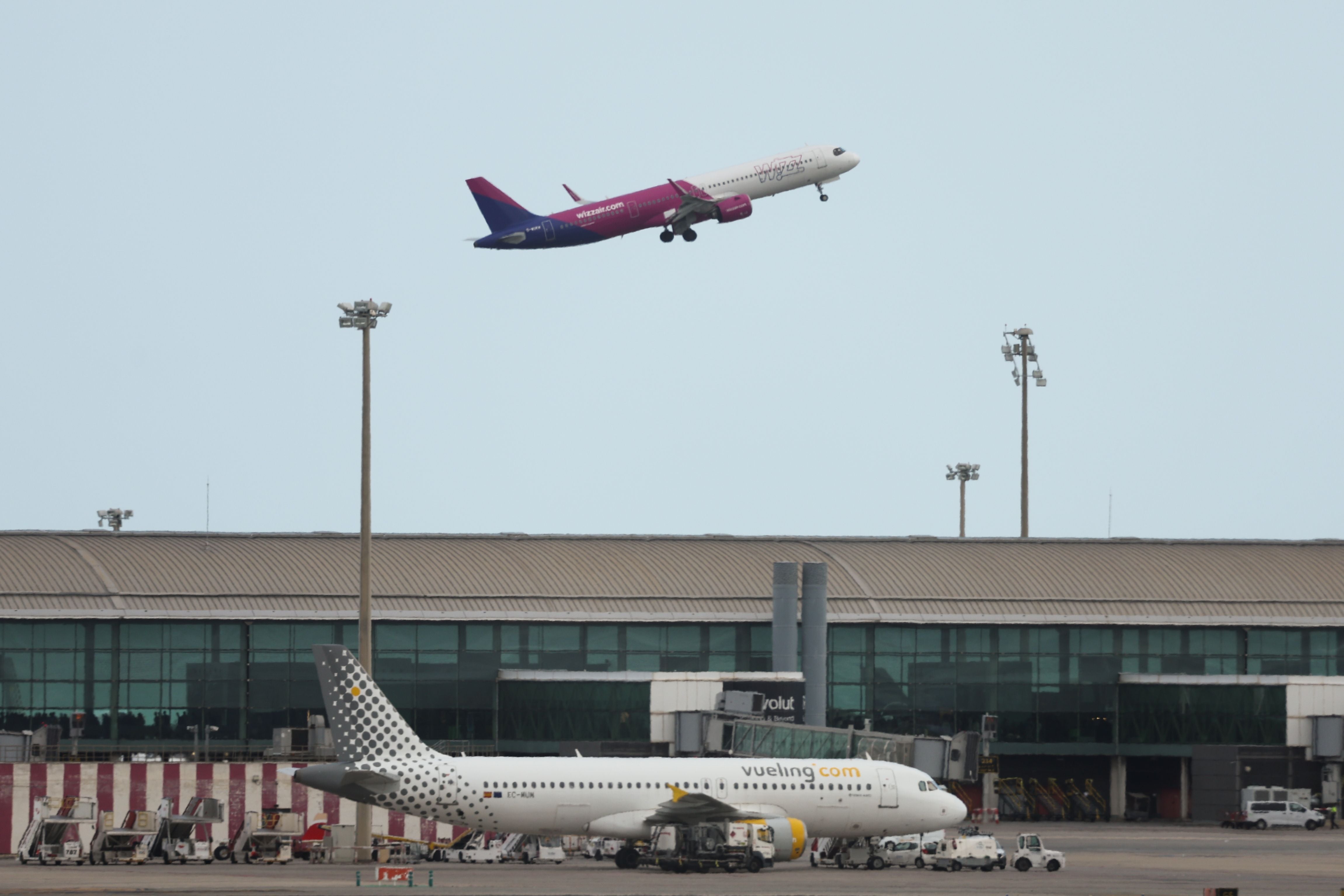 Eine Wizz Air Maschine startet, während ein Vueling Flugzeug am Flughafen steht.