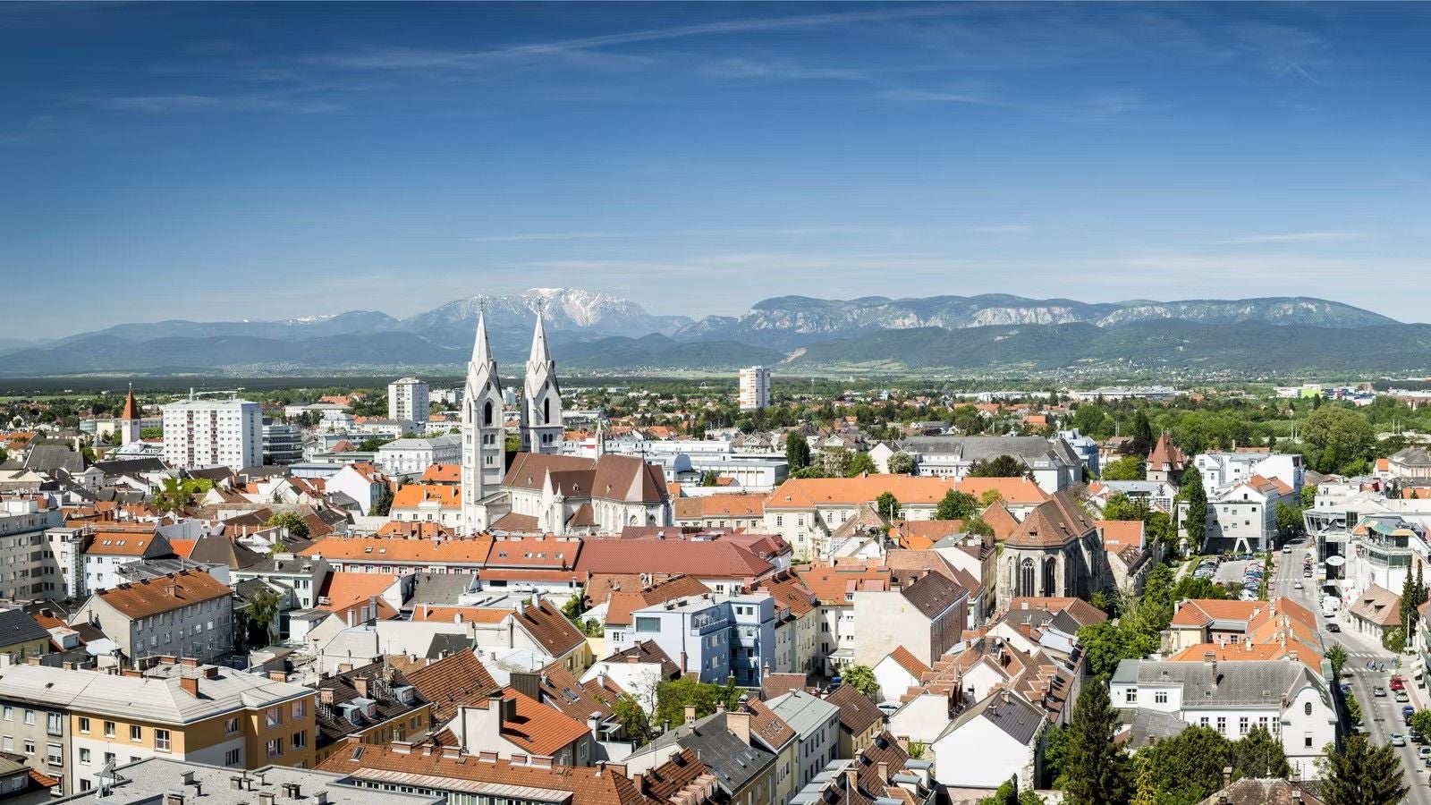 Stadtansicht von Wiener Neustadt mit Kirche, Häusern und Bergen im Hintergrund.