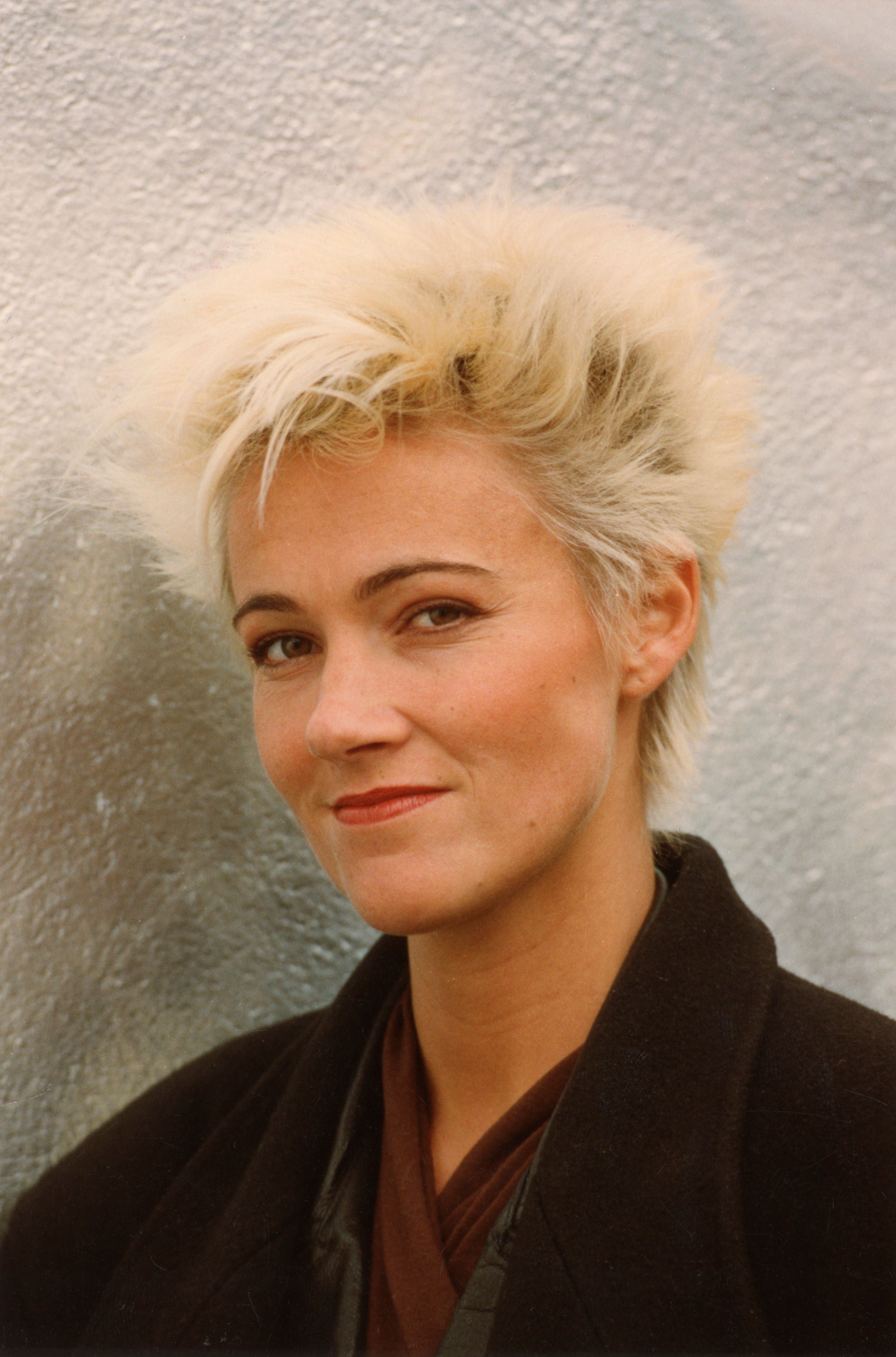 Frau mit kurzen, blonden Haaren und dunkler Jacke vor heller Wand, 1989 fotografiert.