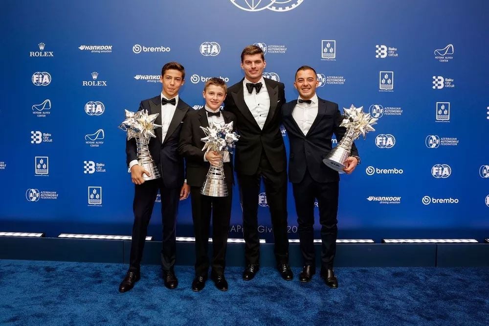 Vier Männer in Anzügen posieren mit großen Trophäen vor einer blauen FIA-Hintergrundwand.