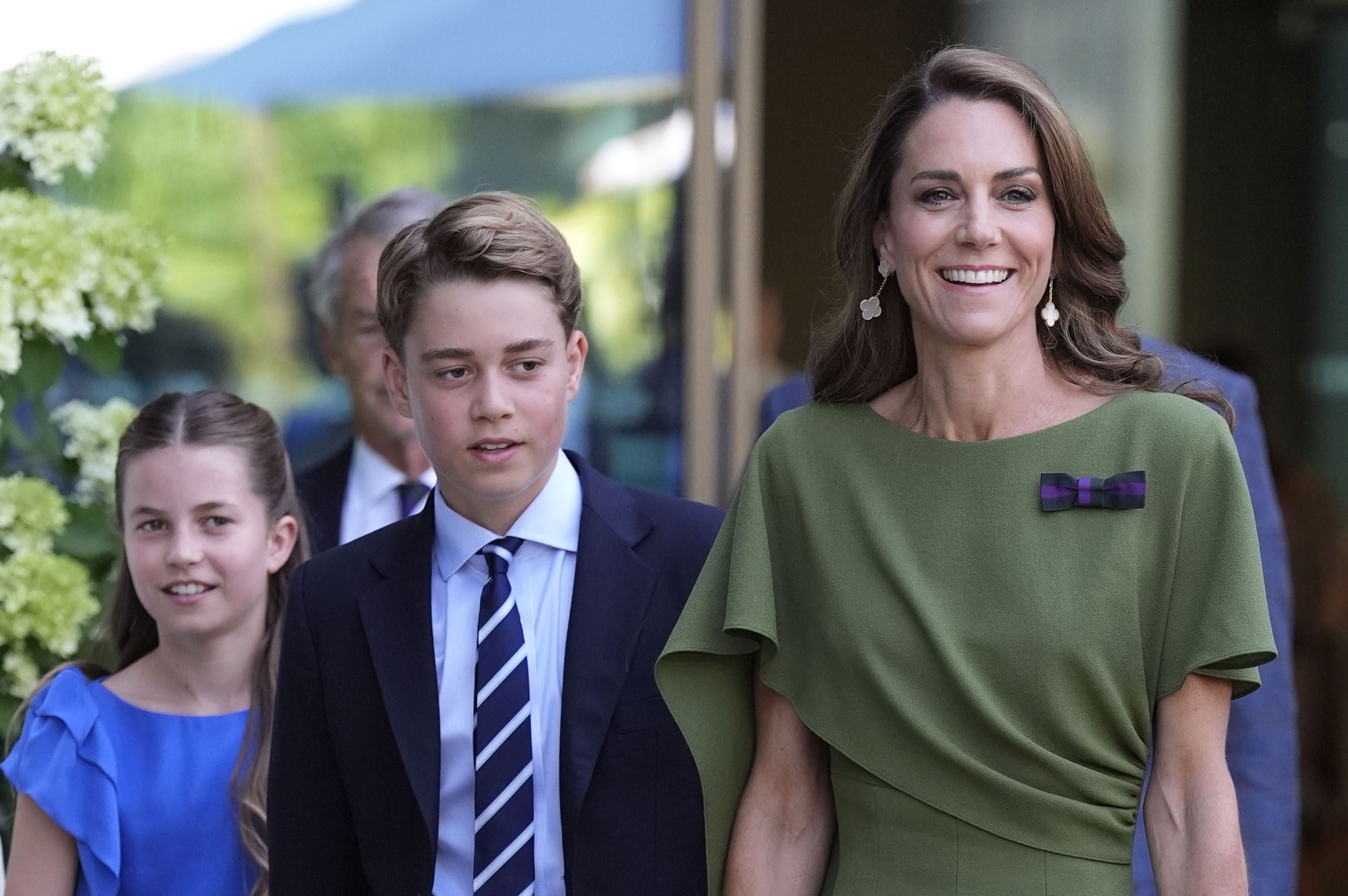 Eine Frau und zwei Kinder gehen elegant gekleidet nebeneinander und lächeln.