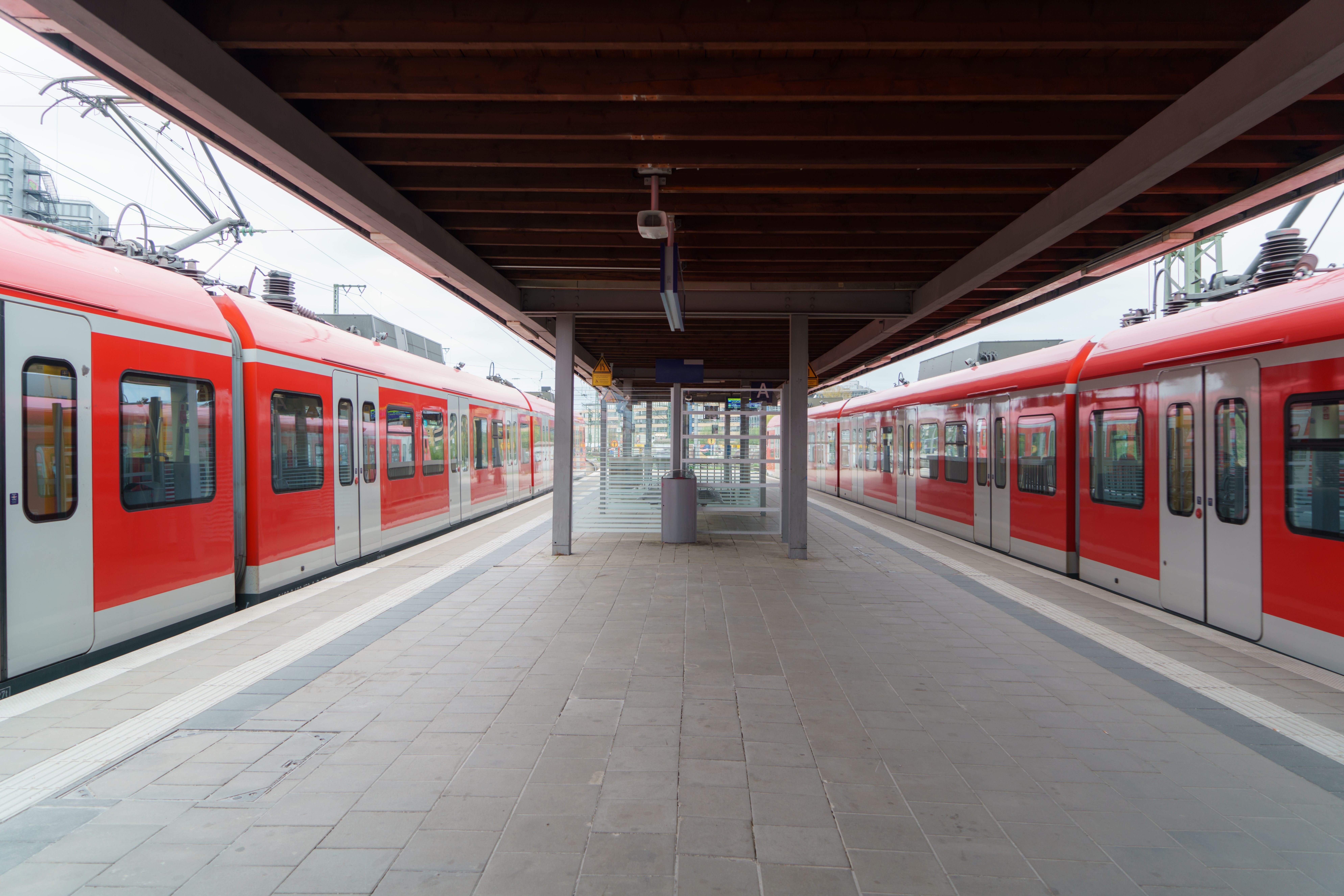 Leerer Bahnsteig mit zwei roten S-Bahnen unter einem Holzdach an einem modernen Bahnhof.