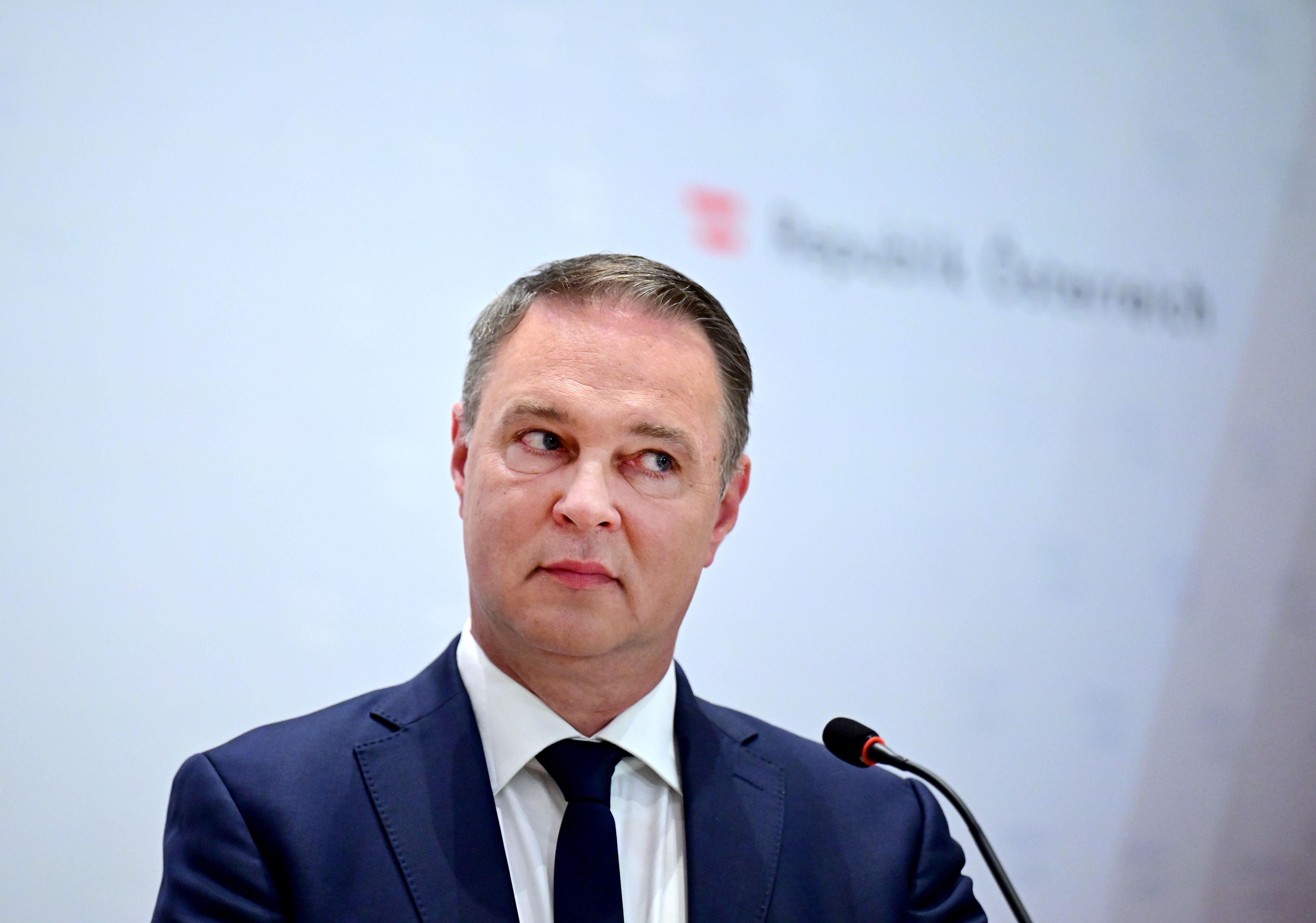 Ein Mann im Anzug spricht ernst bei einer Pressekonferenz mit Mikrofon.