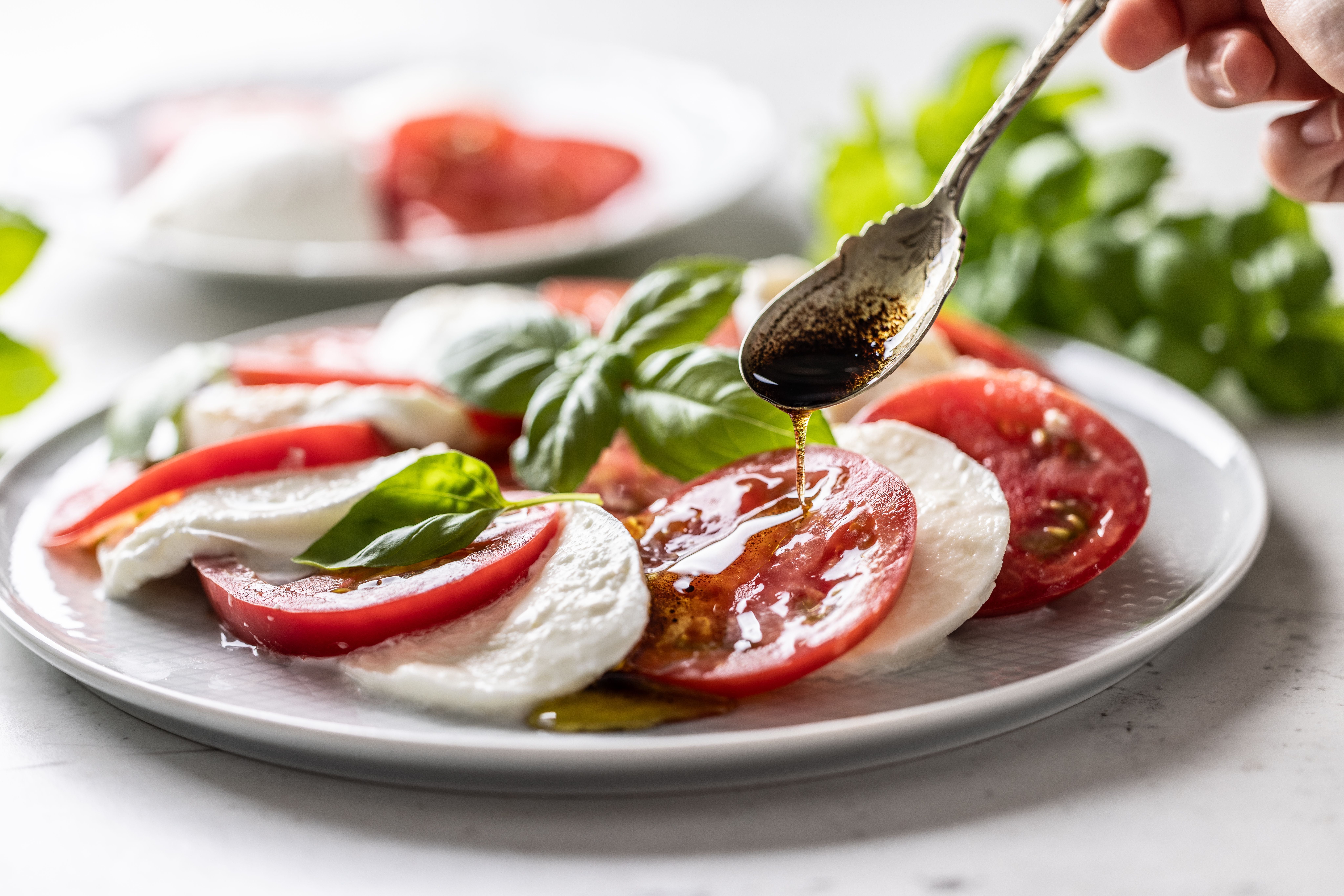 Caprese-Salat mit Tomaten, Mozzarella und Basilikum, beträufelt mit Balsamico-Dressing.