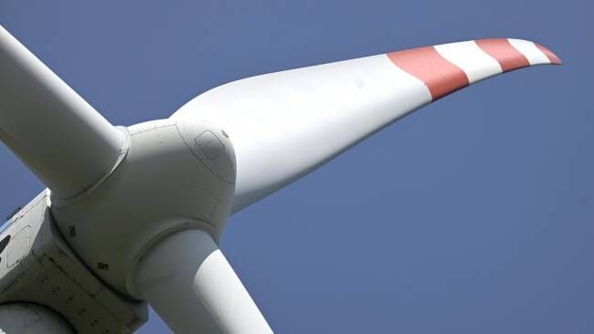 Nahaufnahme eines Windradflügels mit rotem Streifen vor blauem Himmel.