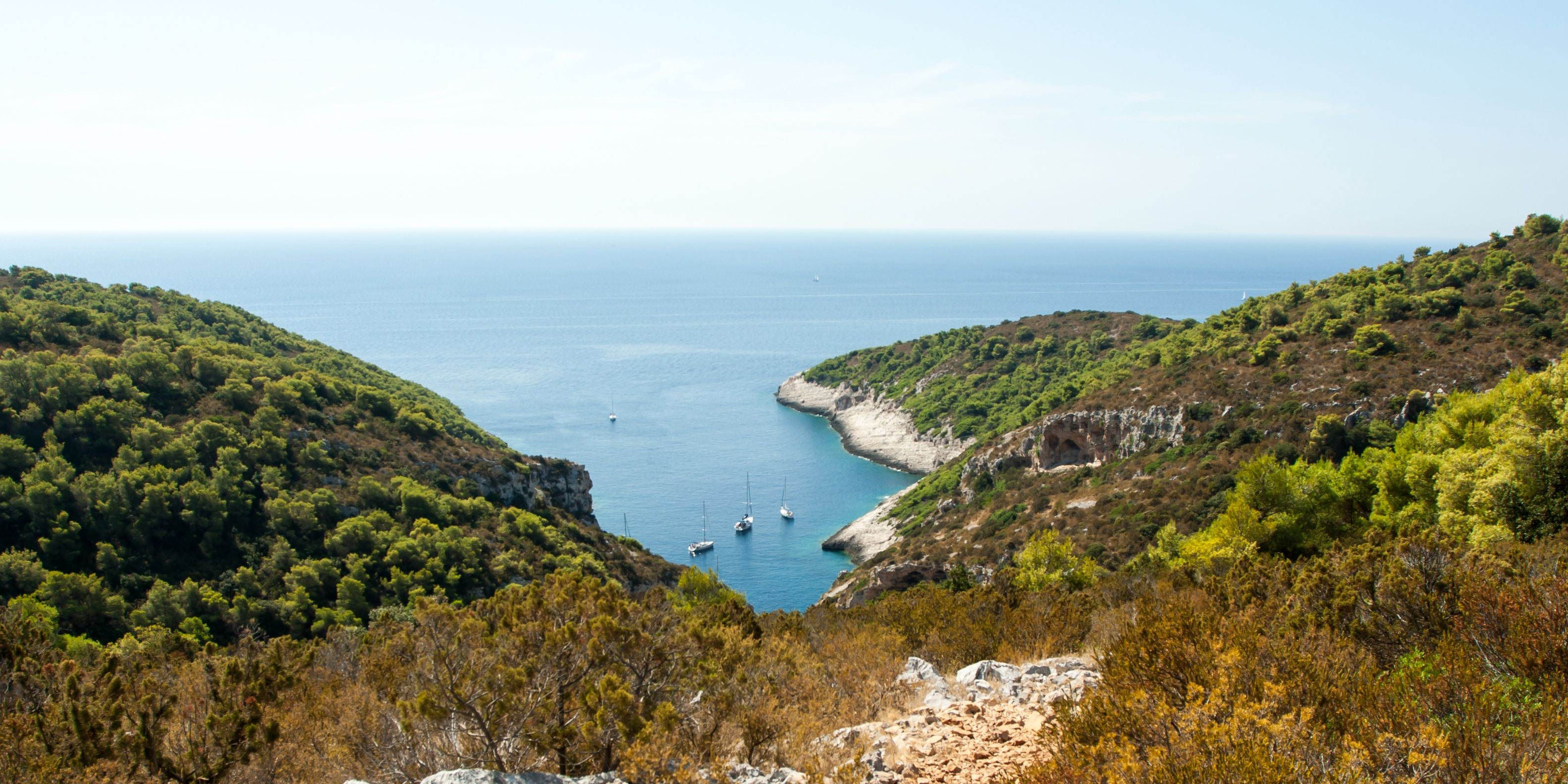 Blick auf eine Bucht mit Segelbooten, umgeben von grünen Hügeln auf der Insel Vis, Kroatien.