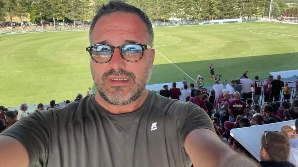 Mann mit Brille macht Selfie im Fußballstadion, Zuschauer und Spielfeld im Hintergrund.
