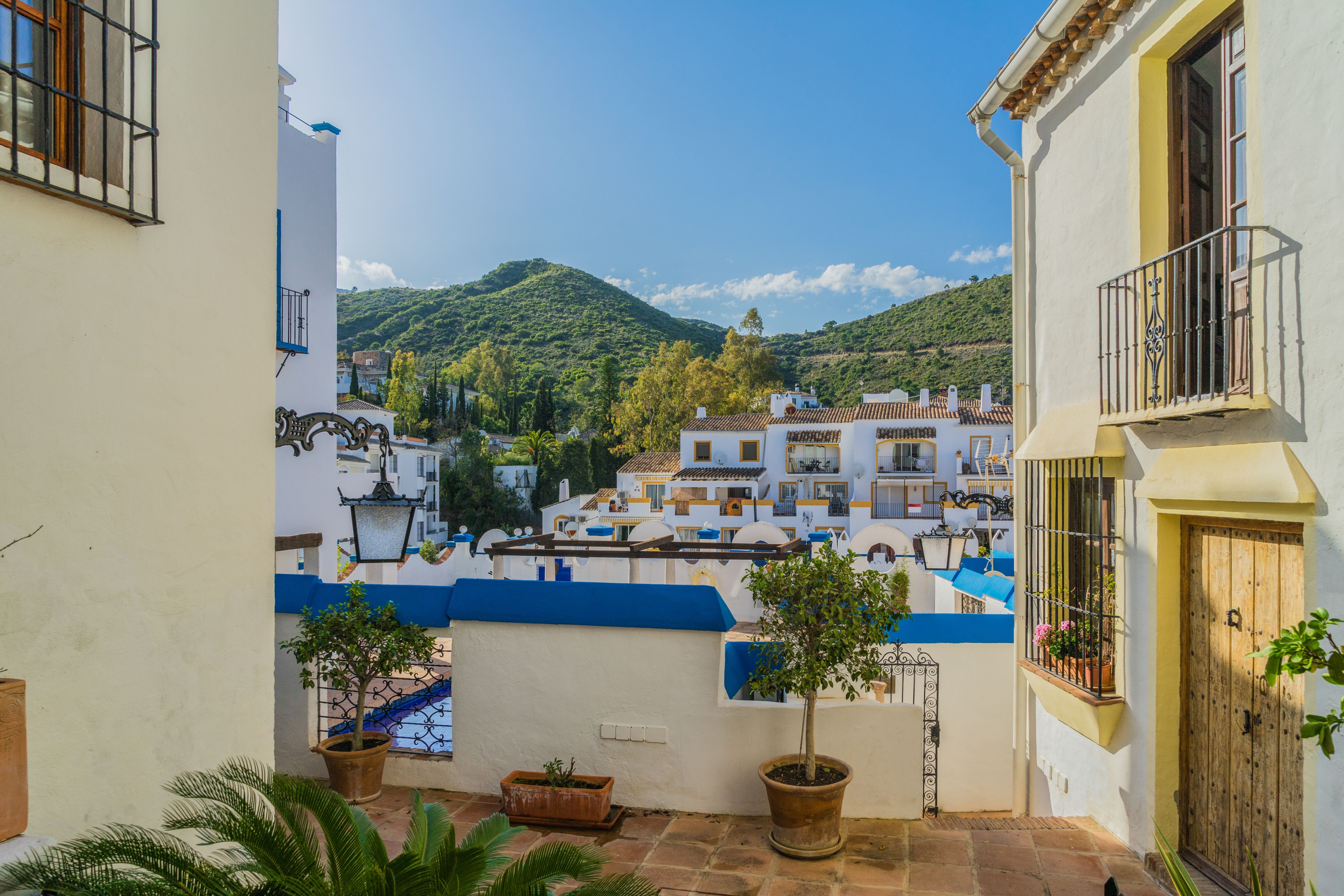 Blick auf weiße Häuser eines andalusischen Dorfs mit Bergen im Hintergrund und sonnigem Himmel.