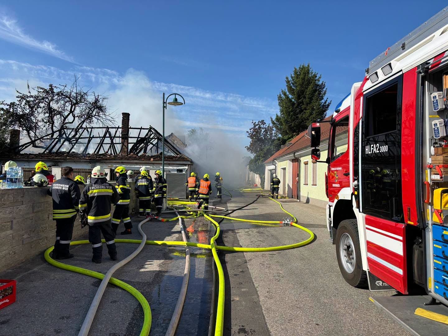 Feuerwehr bekämpft Brand in einem Wohnhaus, Rauch steigt auf, mehrere Einsatzkräfte vor Ort.