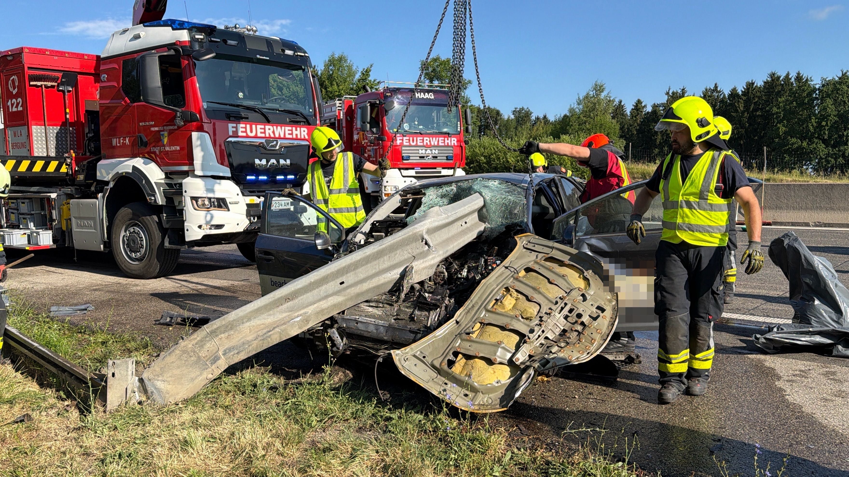 Feuerwehrleute bergen ein stark zerstörtes Auto mit Leitplanke nach schwerem Unfall auf der Straße.
