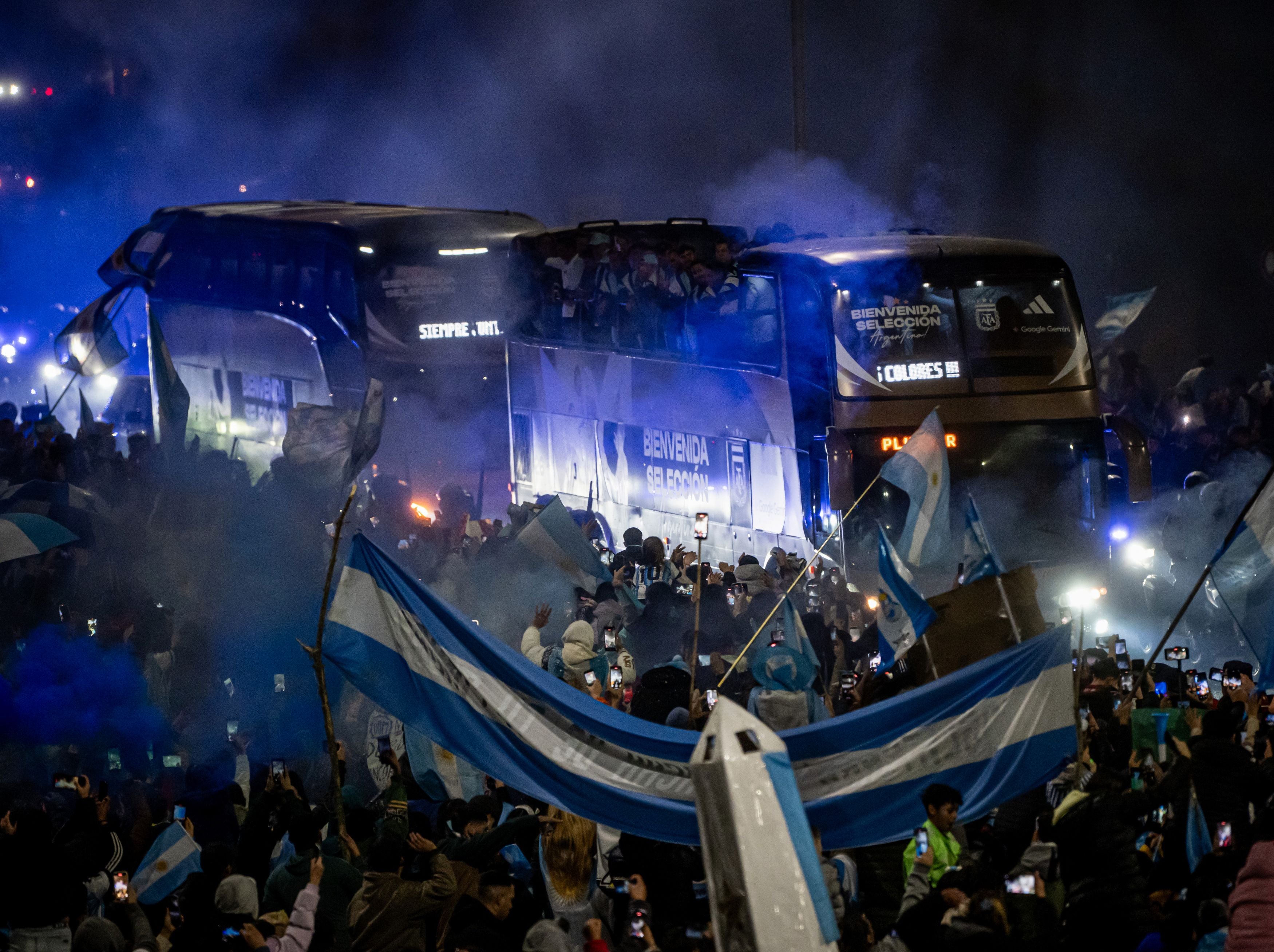 Menschenmenge mit argentinischen Fahnen empfängt Busse mit Fußballspielern in Ezeiza bei Nacht.