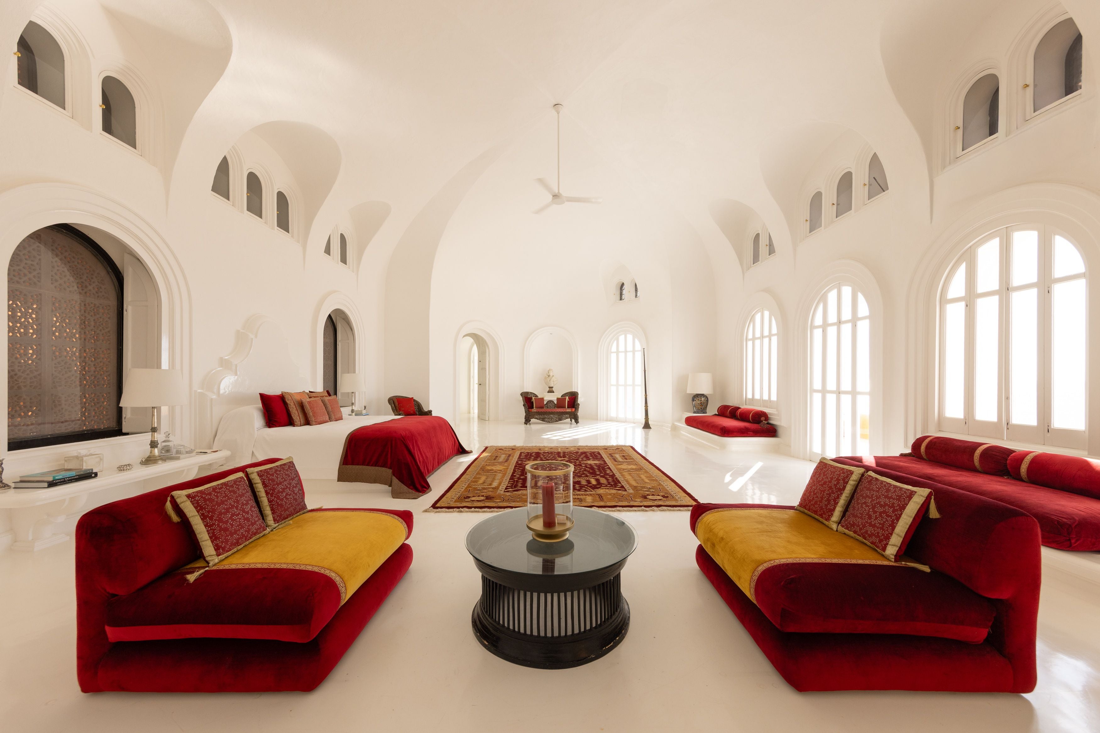 Helles Wohnzimmer mit roten und gelben Sofas, weißen Wänden und großen Fenstern im mediterranen Stil.