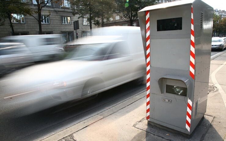 Ein Blitzer am Straßenrand fotografiert ein vorbeifahrendes, verschwommenes Auto.