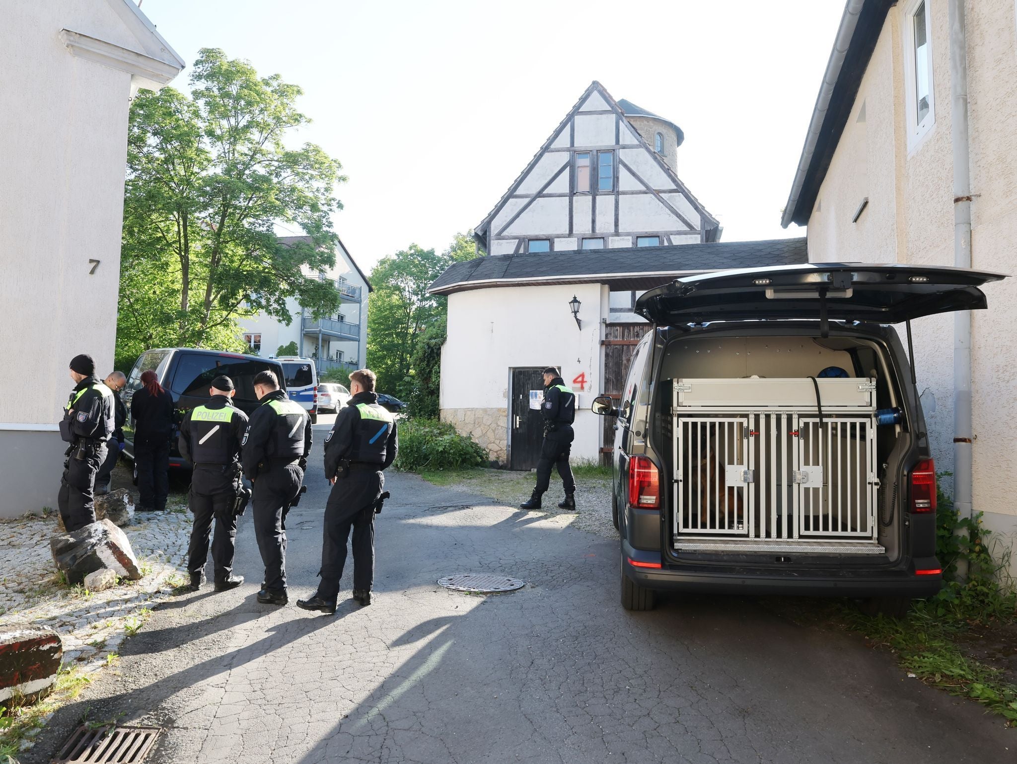 Polizisten und Hundestaffel durchsuchen ein Gebäude mit Polizeifahrzeugen in einer Wohnstraße.