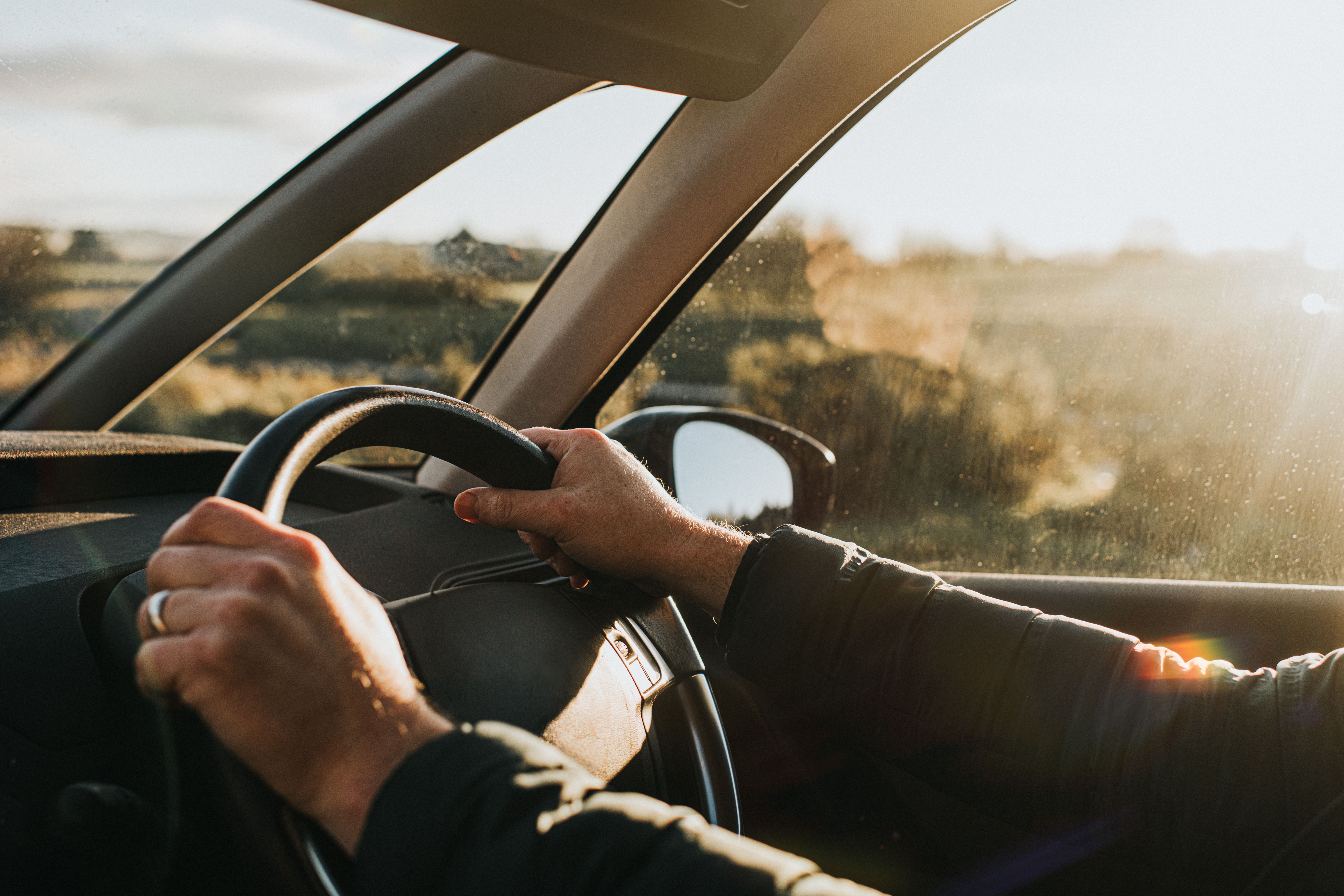 Hände am Lenkrad eines Autos, Sonnenlicht scheint durch das Fenster bei Sonnenuntergang.