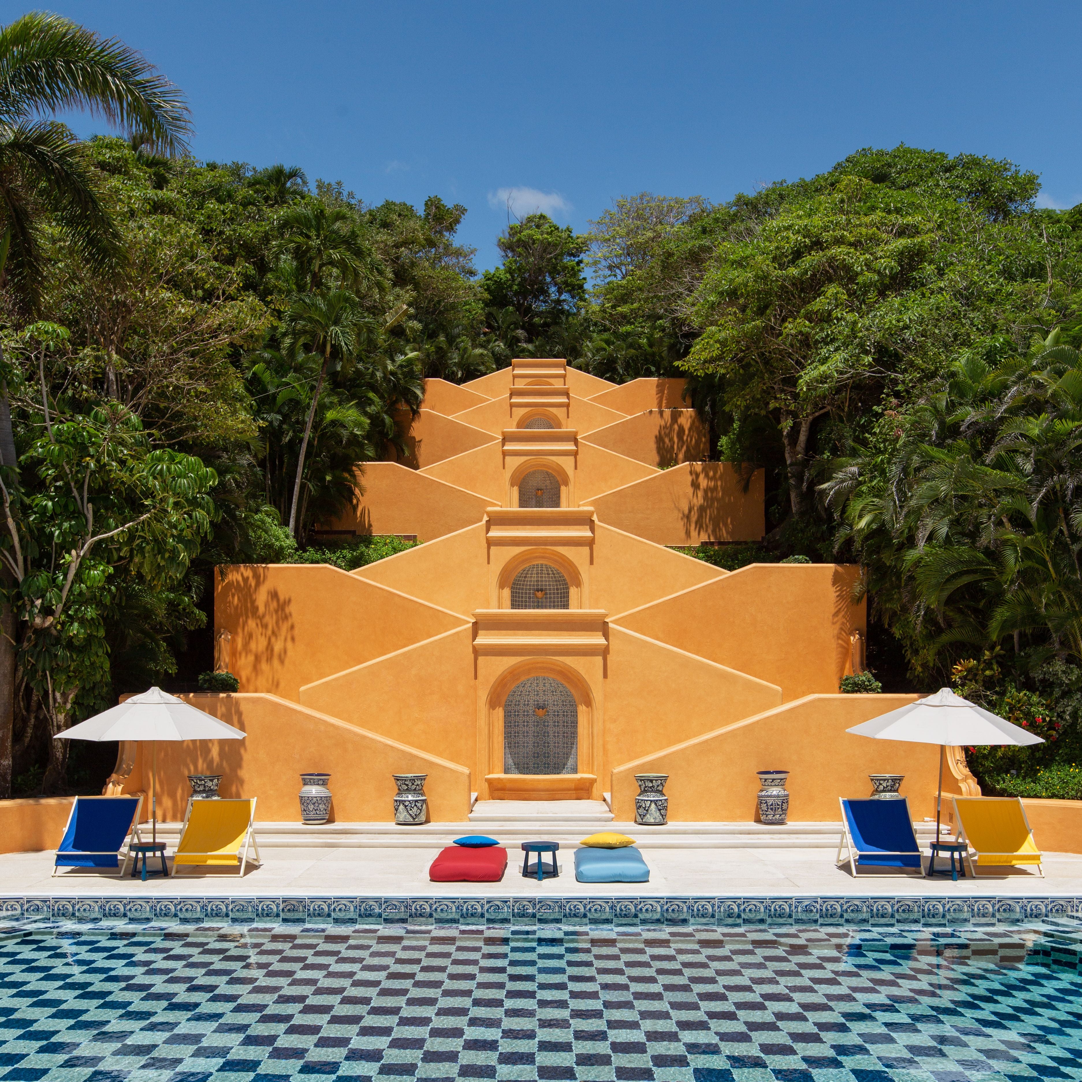 Bunte Poolliegen und Sonnenschirme vor einer gelben Treppenanlage im Grünen in Cuixmala.