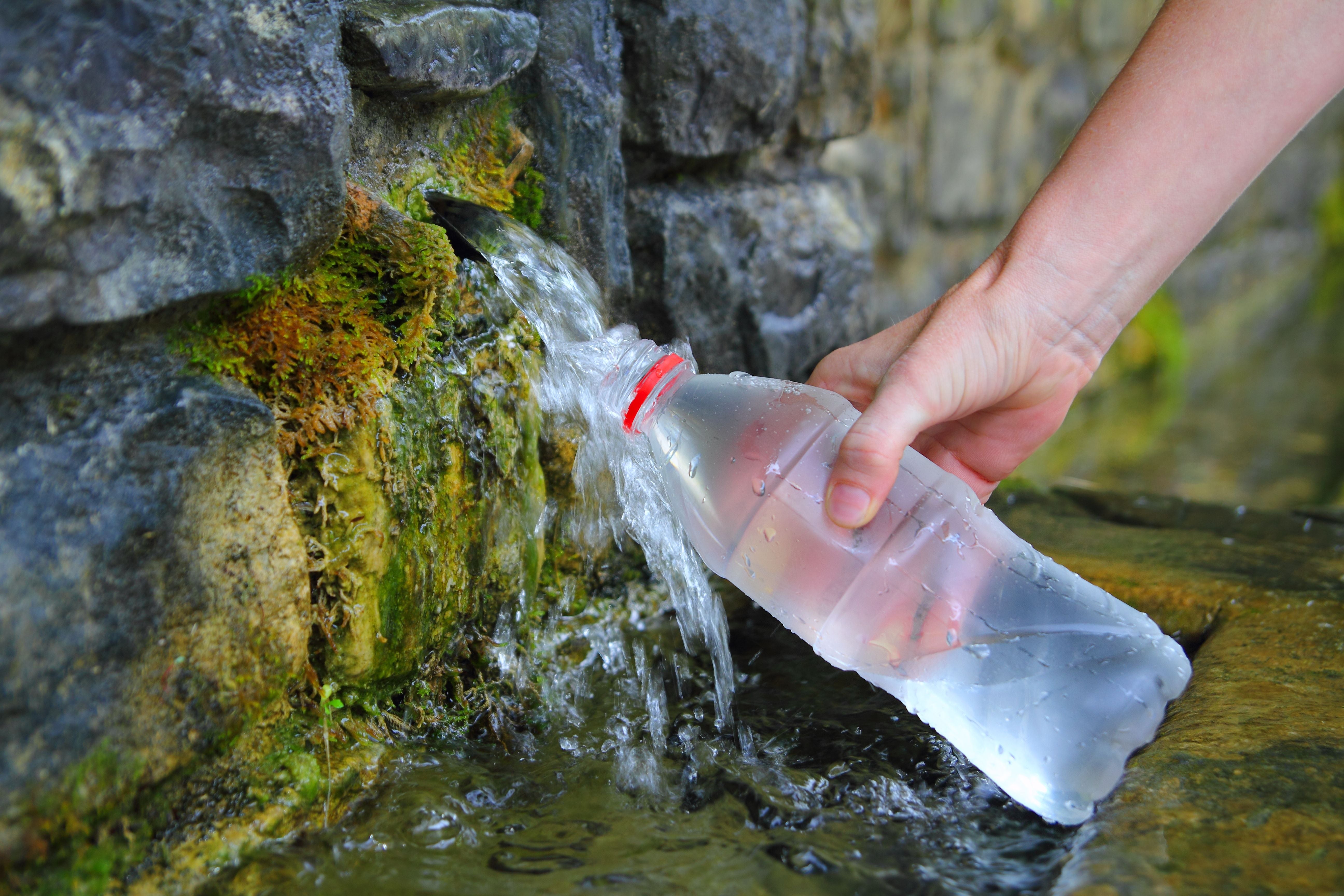 Hand füllt eine Plastikflasche mit Quellwasser aus einem Felsen in den Pyrenäen.
