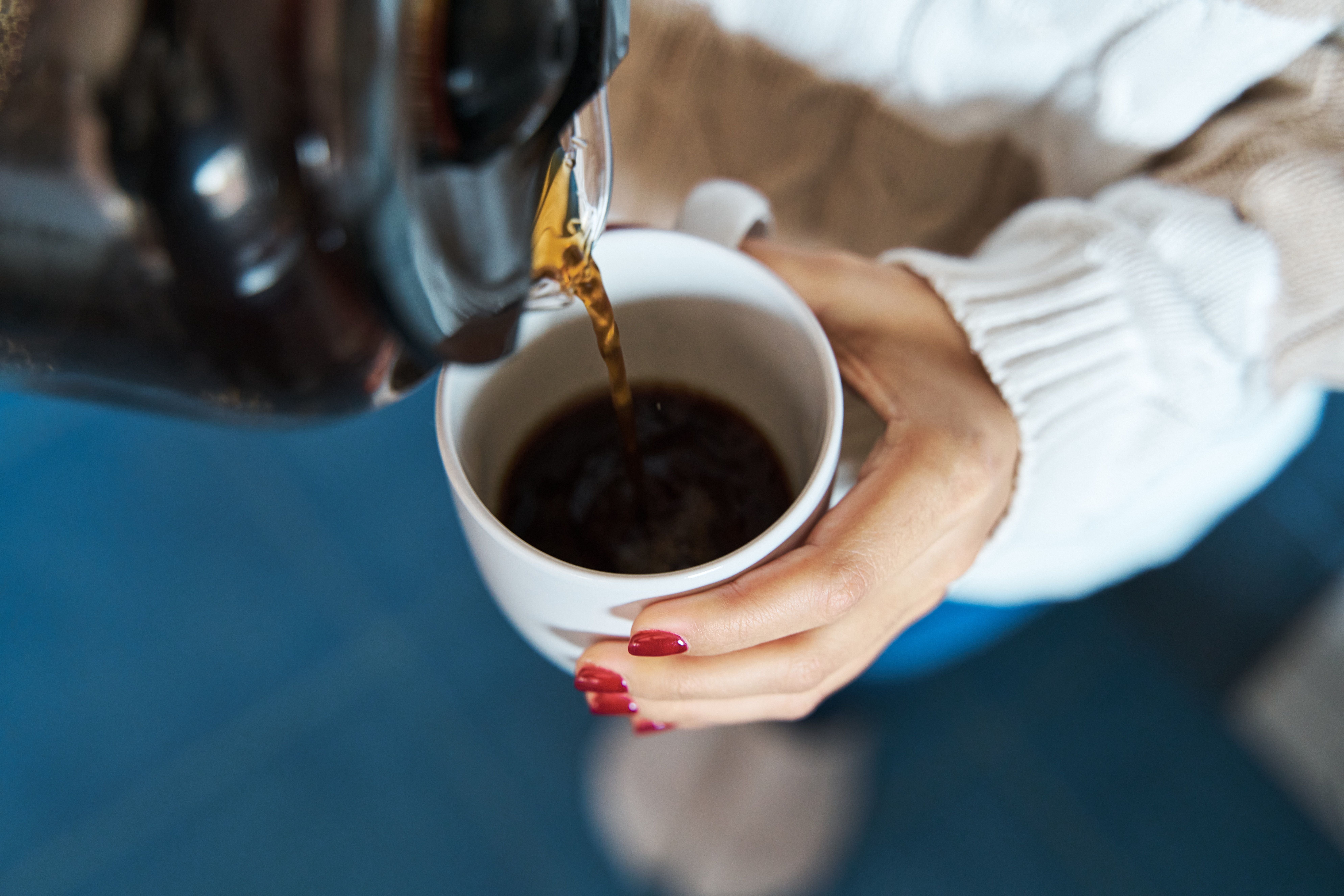 Nahaufnahme: Eine Frau schenkt sich zu Hause Filterkaffee in eine weiße Tasse ein.