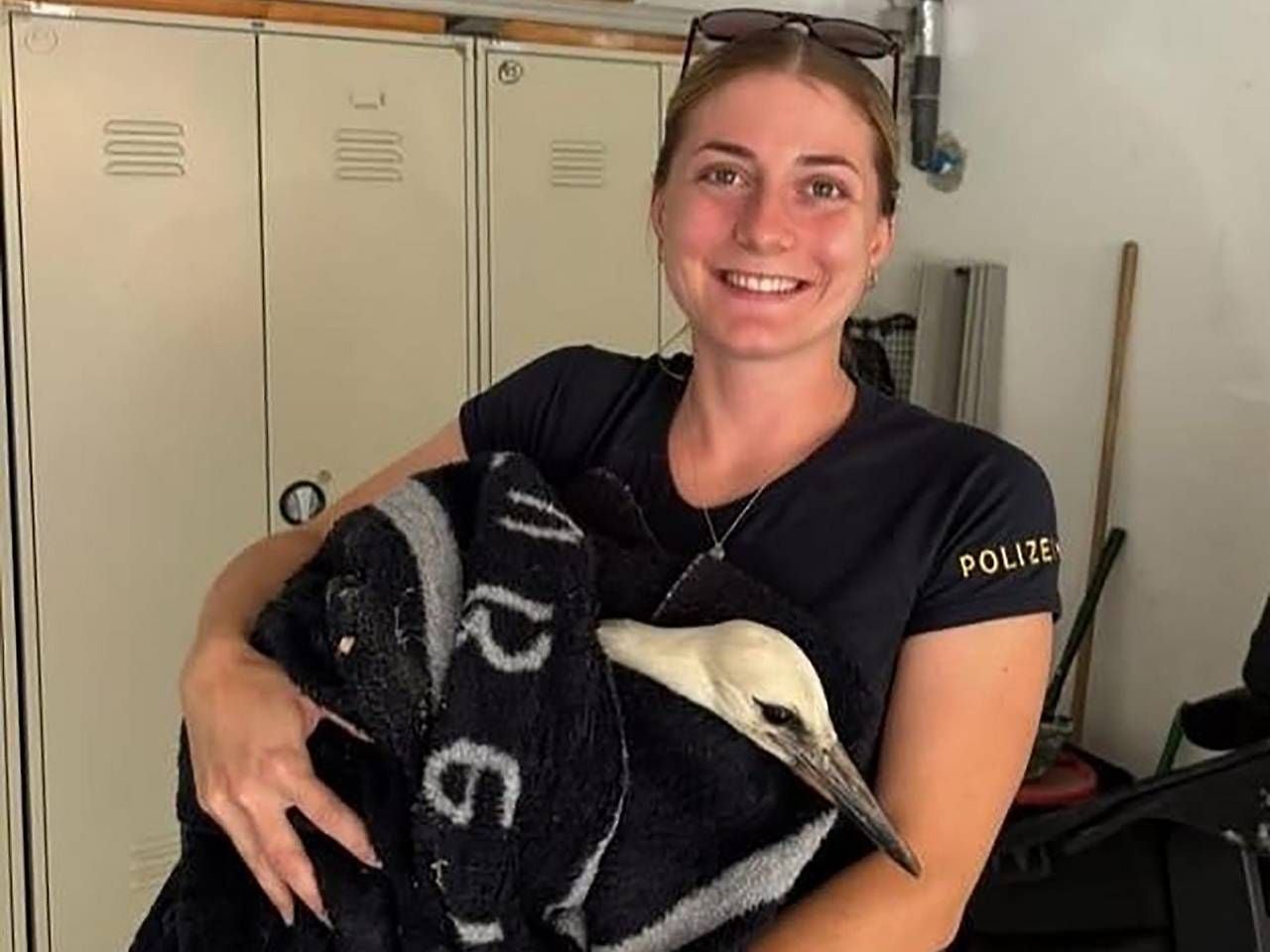 Polizistin hält einen in eine Decke gewickelten Baby-Storch und lächelt in die Kamera.