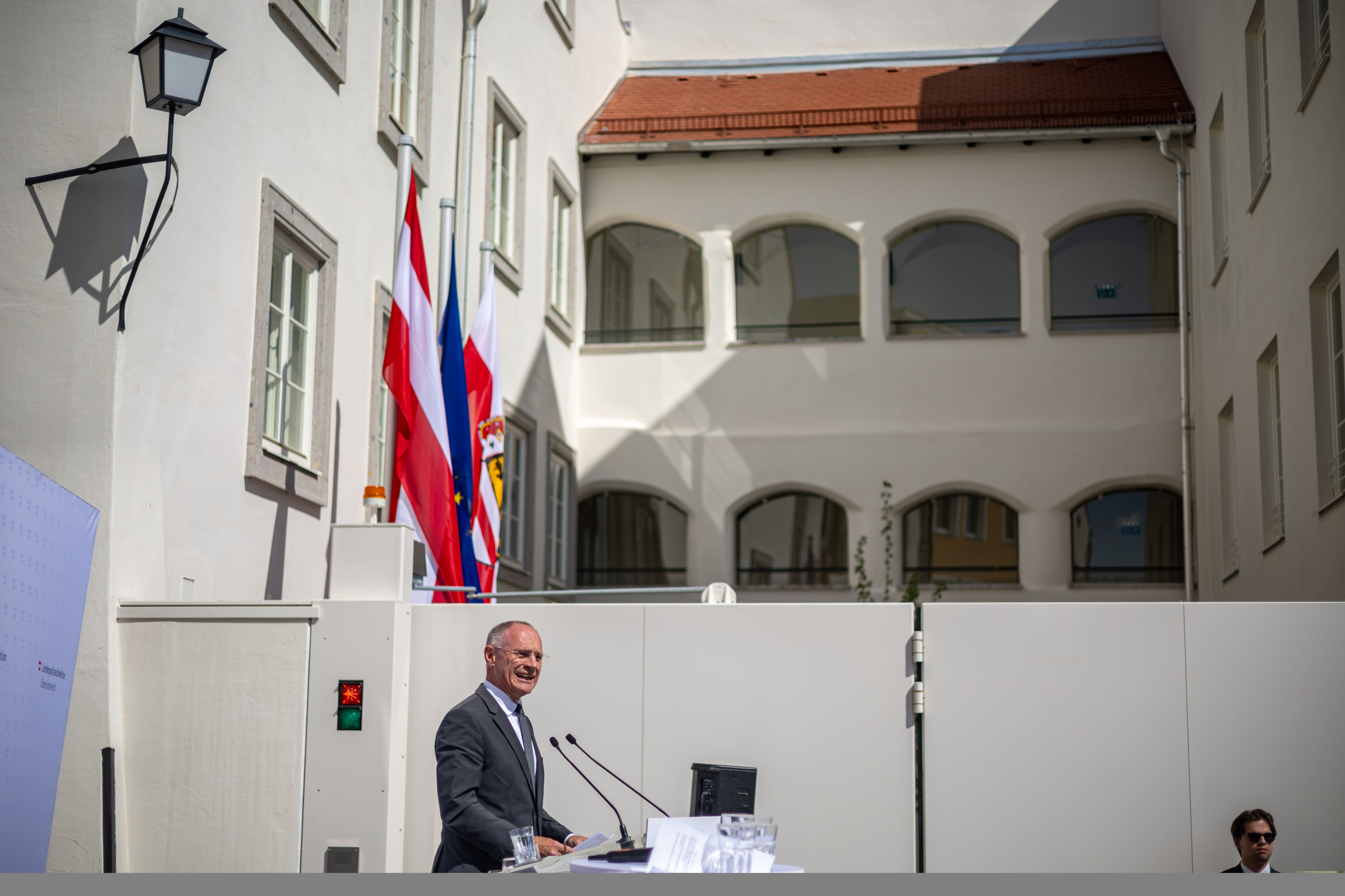 Ein Mann hält eine Rede vor einer Polizei­station mit österreichischen Fahnen im Innenhof eines Gebäudes.