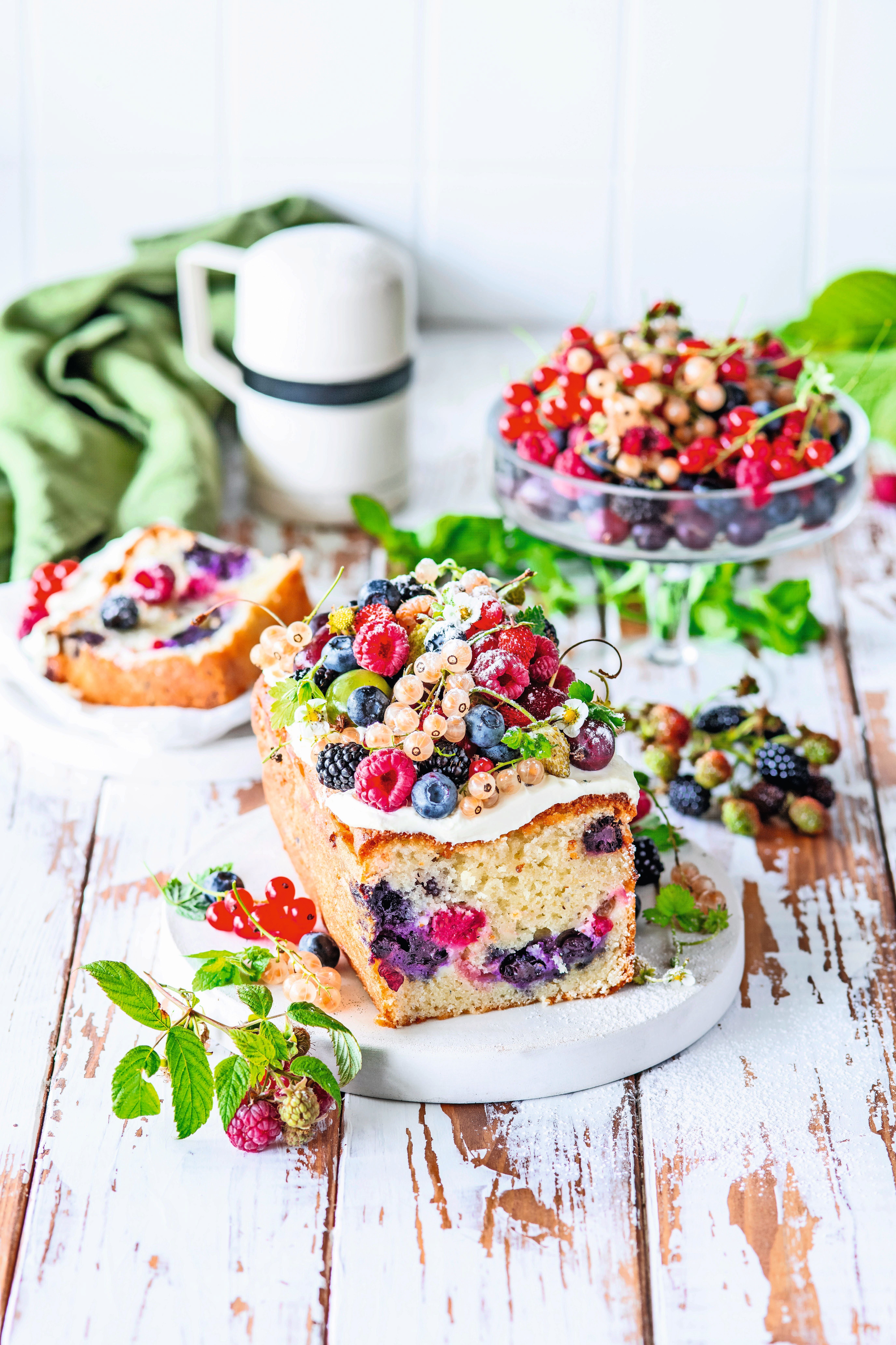 Sommerlicher Kastenkuchen mit bunten Beeren auf einem weißen Holztisch angerichtet.