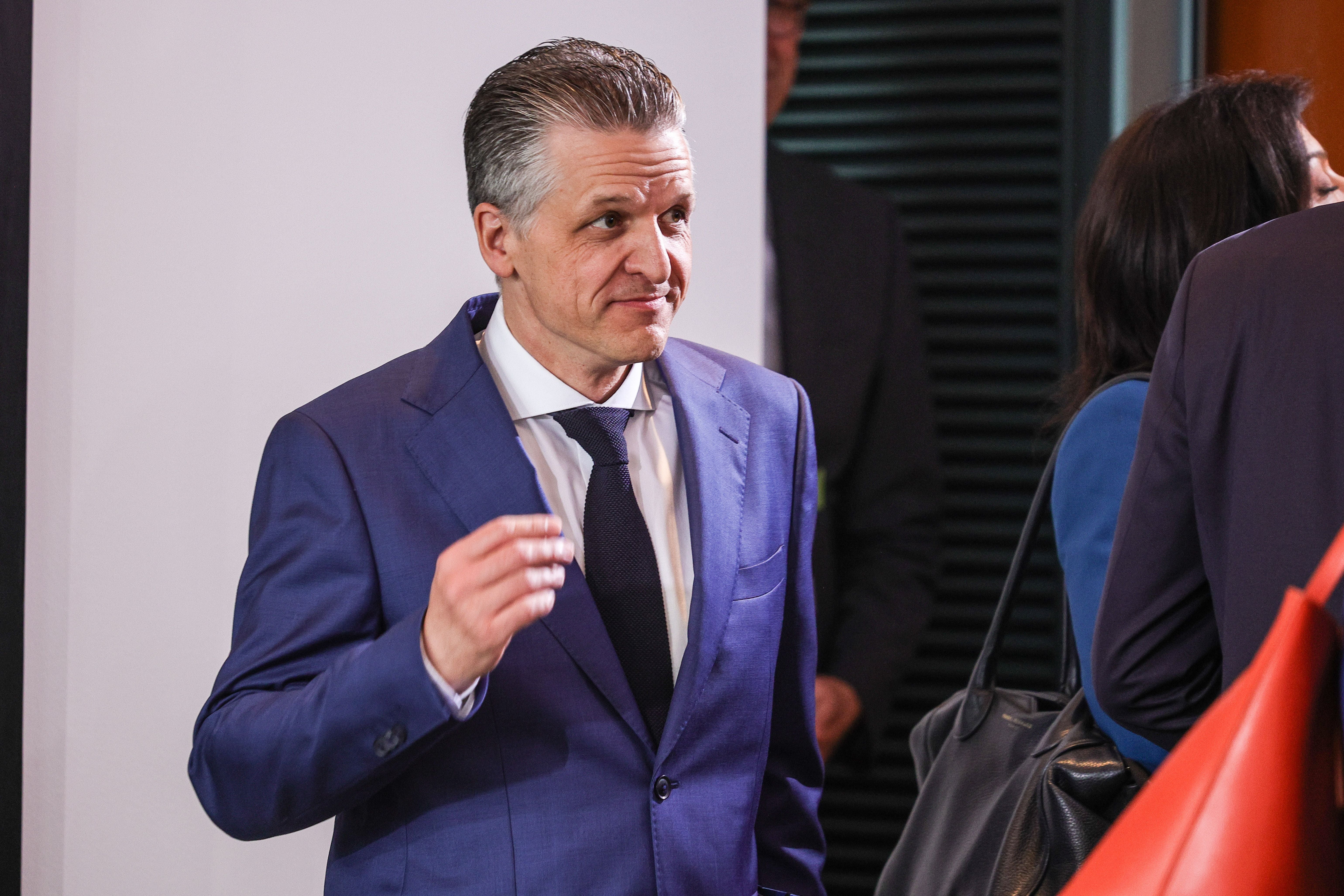 Ein Mann im blauen Anzug bei einer Veranstaltung, im Gespräch mit anderen Personen.