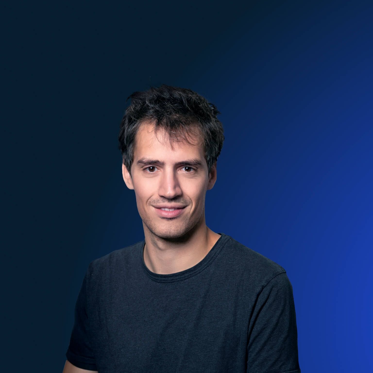 Junger Mann mit dunklem Haar und T-Shirt vor blauem Hintergrund.