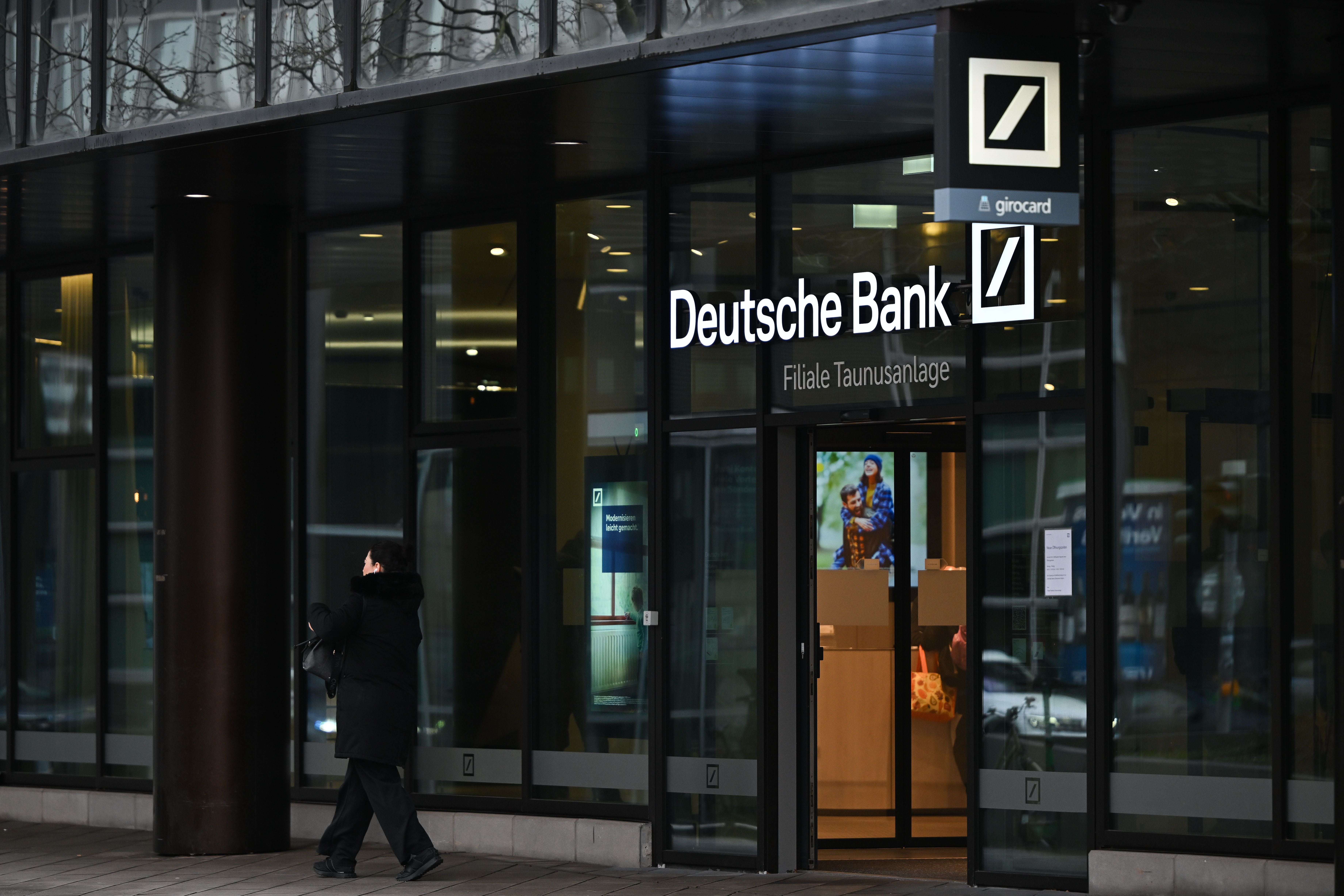 Eine Person läuft an einer Glasfassade der Deutsche Bank Filiale in Frankfurt vorbei.