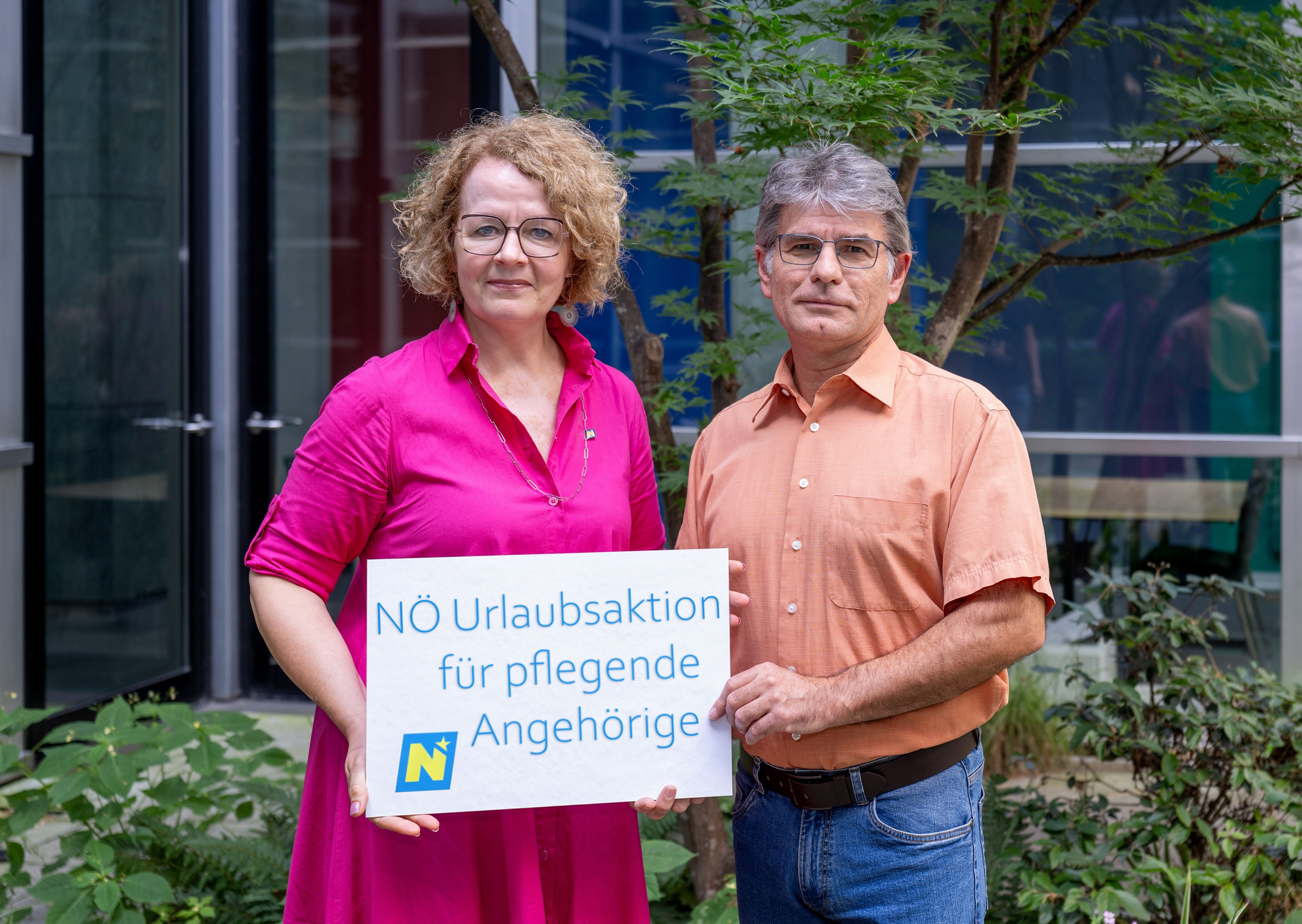 Zwei Personen halten ein Schild mit der Aufschrift „NÖ Urlaubsaktion für pflegende Angehörige“.
