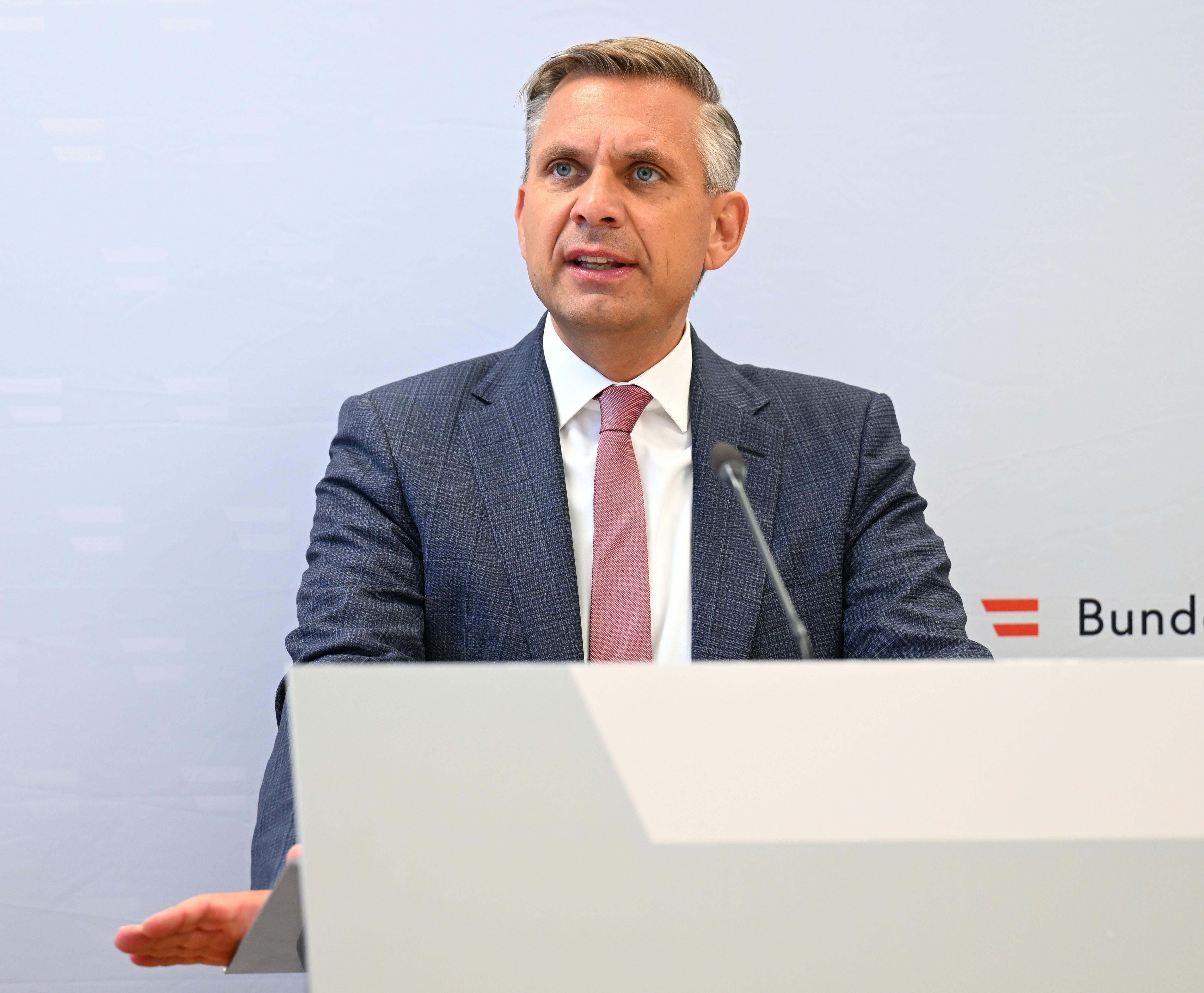 Ein Mann im Anzug spricht auf einer Pressekonferenz mit Mikrofon und Rednerpult.