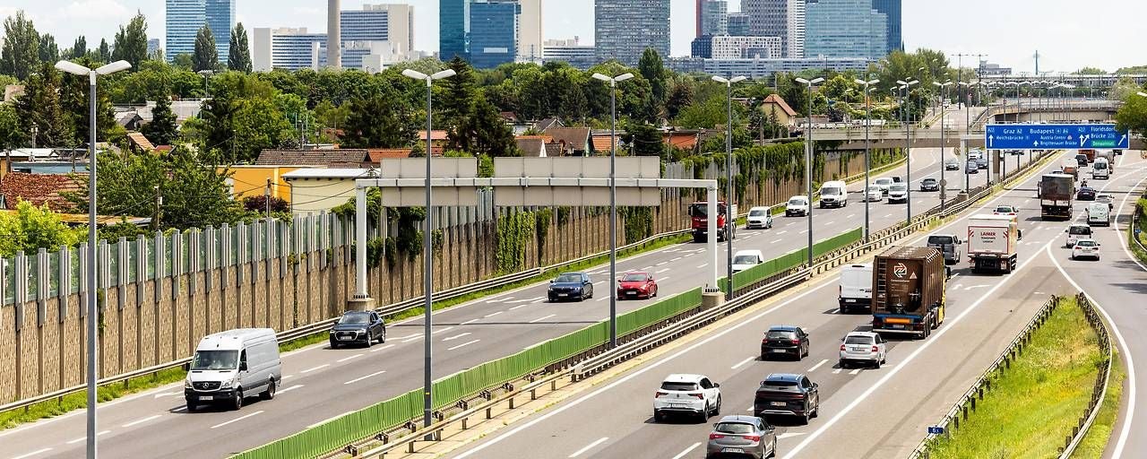 Mehrspurige Autobahn in Wien mit vielen Autos und Hochhäusern im Hintergrund.