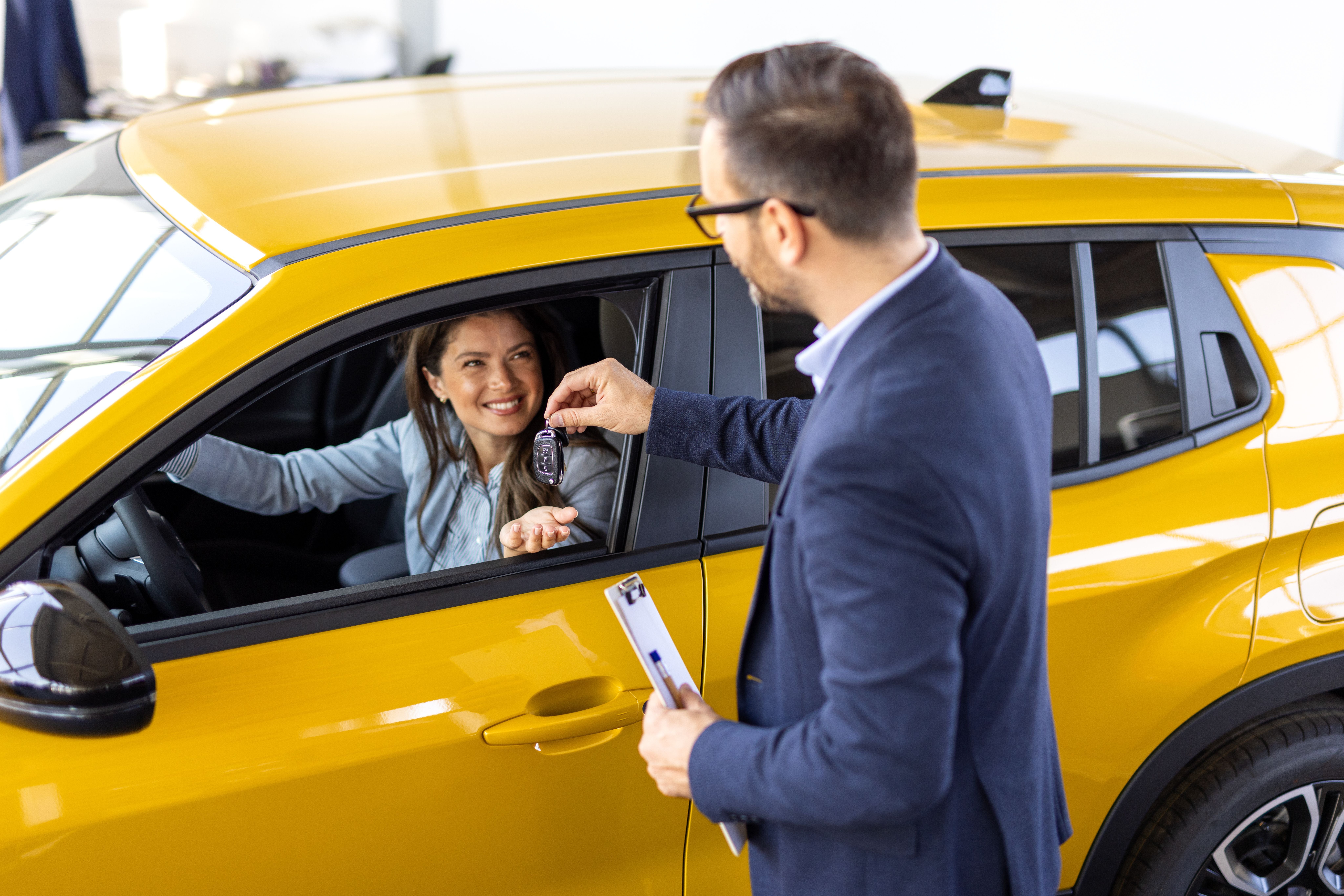 Eine Frau erhält lächelnd Autoschlüssel von einem Mitarbeiter im gelben Mietwagen.