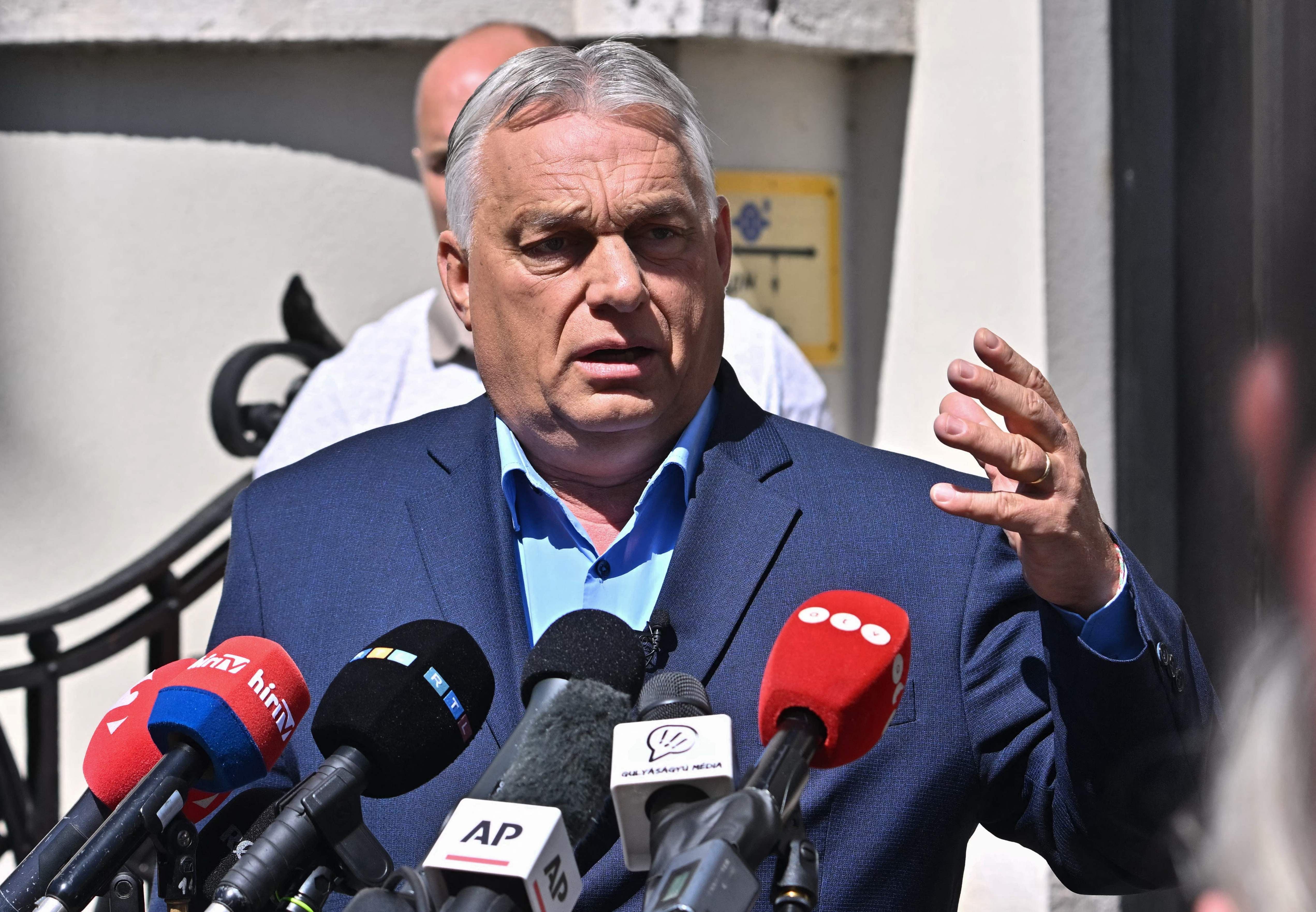 Ein Mann im Anzug spricht auf einer Pressekonferenz vor mehreren Mikrofonen im Freien.