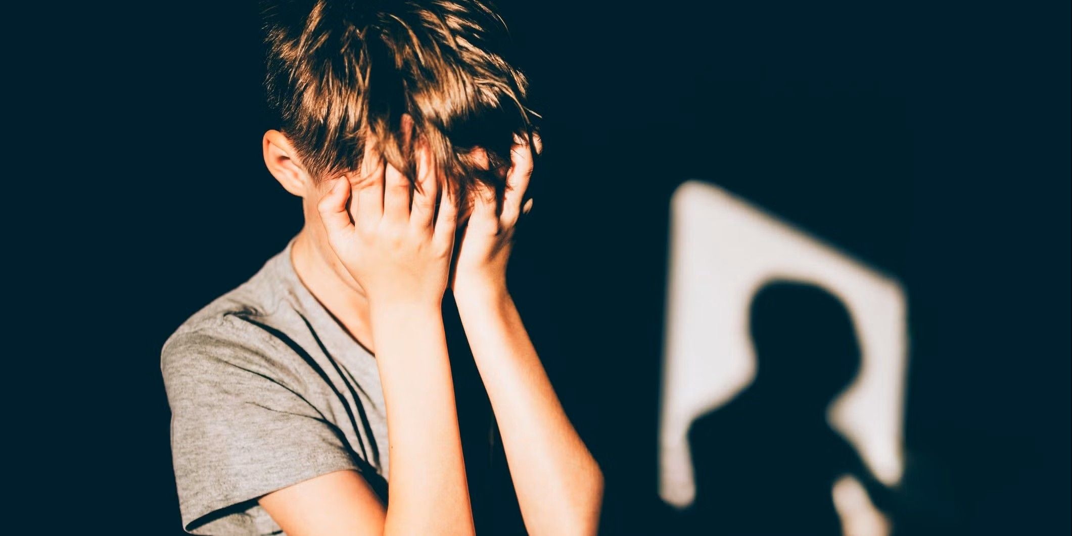 Ein Junge hält sich die Hände vors Gesicht, im Hintergrund ist sein Schatten sichtbar.