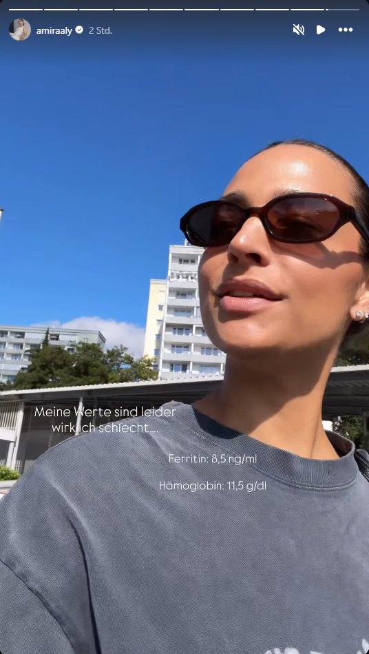 Frau mit Sonnenbrille im Freien, im Hintergrund Wohnhäuser und blauer Himmel.