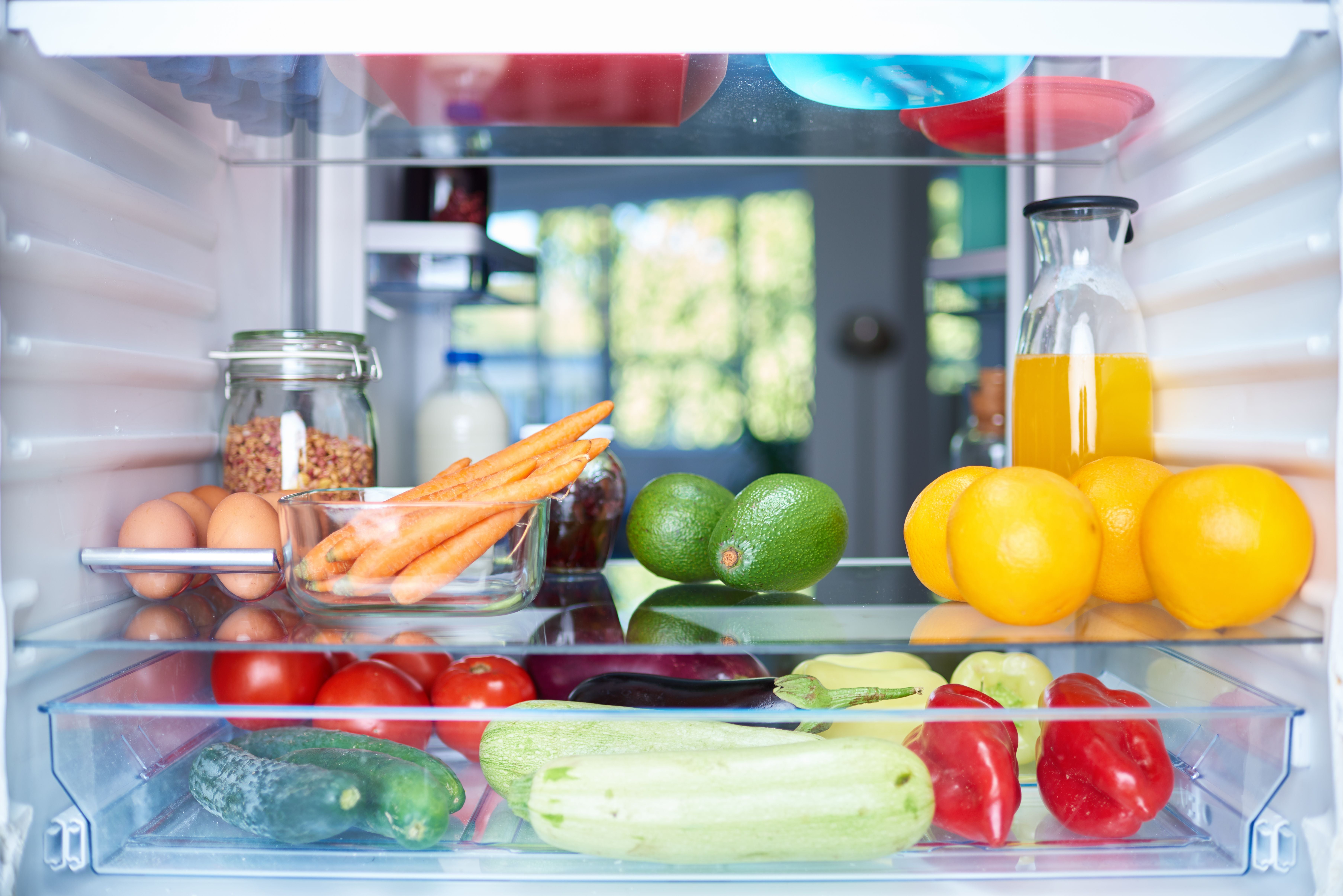 Geöffneter Kühlschrank mit Gemüse, Obst, Eiern, Saft, Milch und einem Glas mit Müsli.