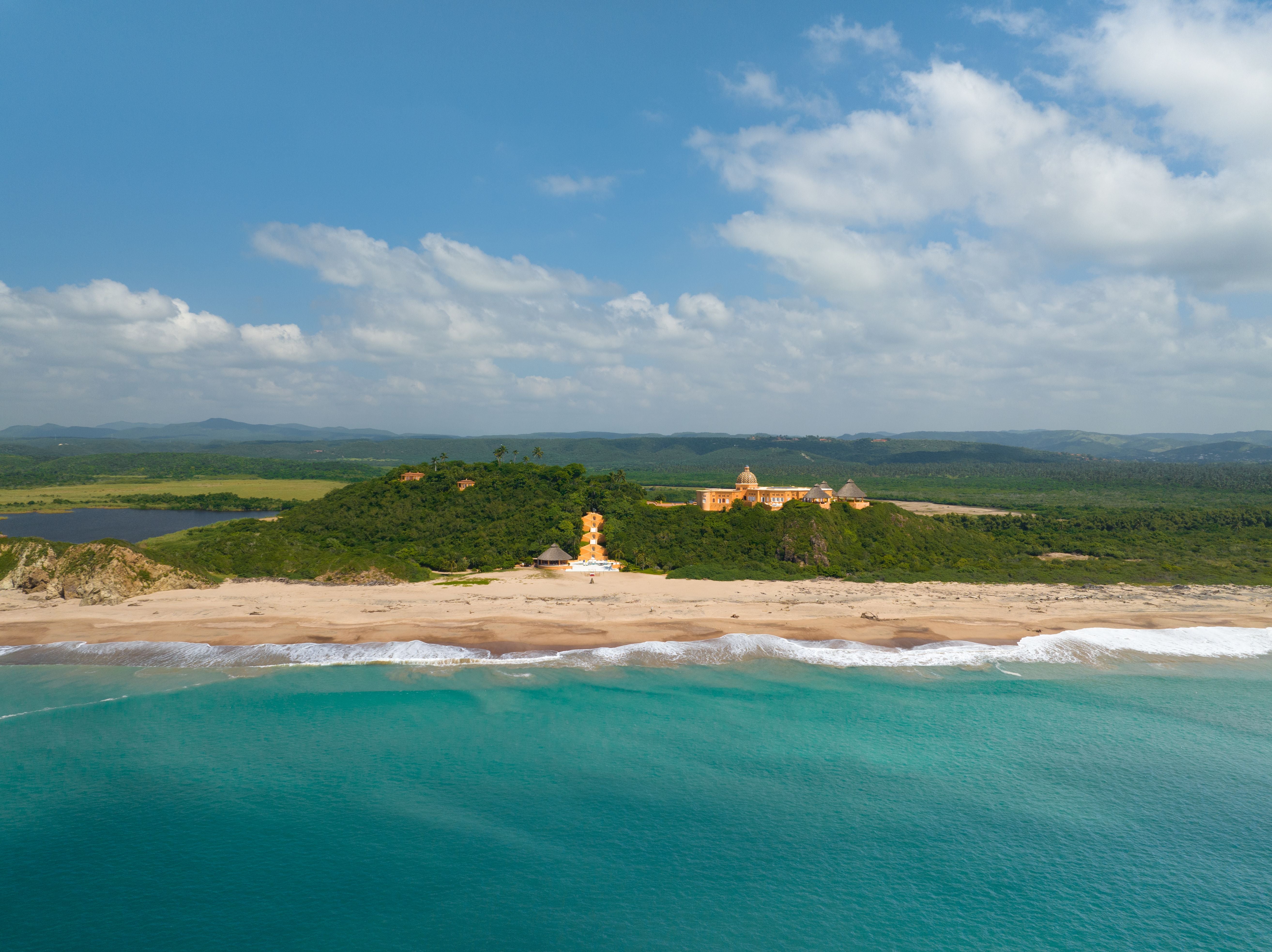Weitläufiger Sandstrand mit türkisfarbenem Meer und grünen Hügeln im Hintergrund bei Cuixmala.