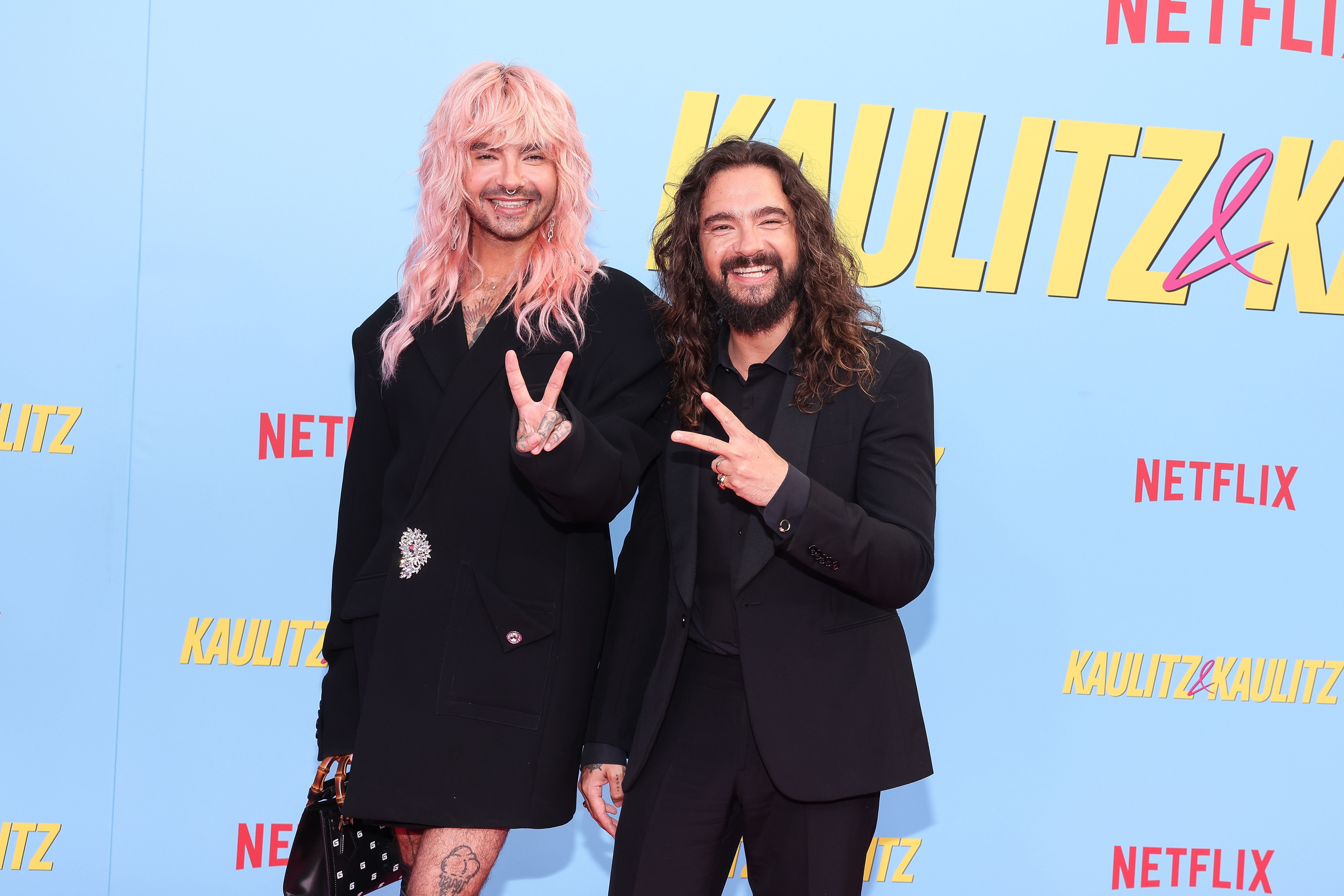 Zwei Männer posieren lachend mit Victory-Zeichen auf einem Netflix-Event in Berlin vor blauem Hintergrund.