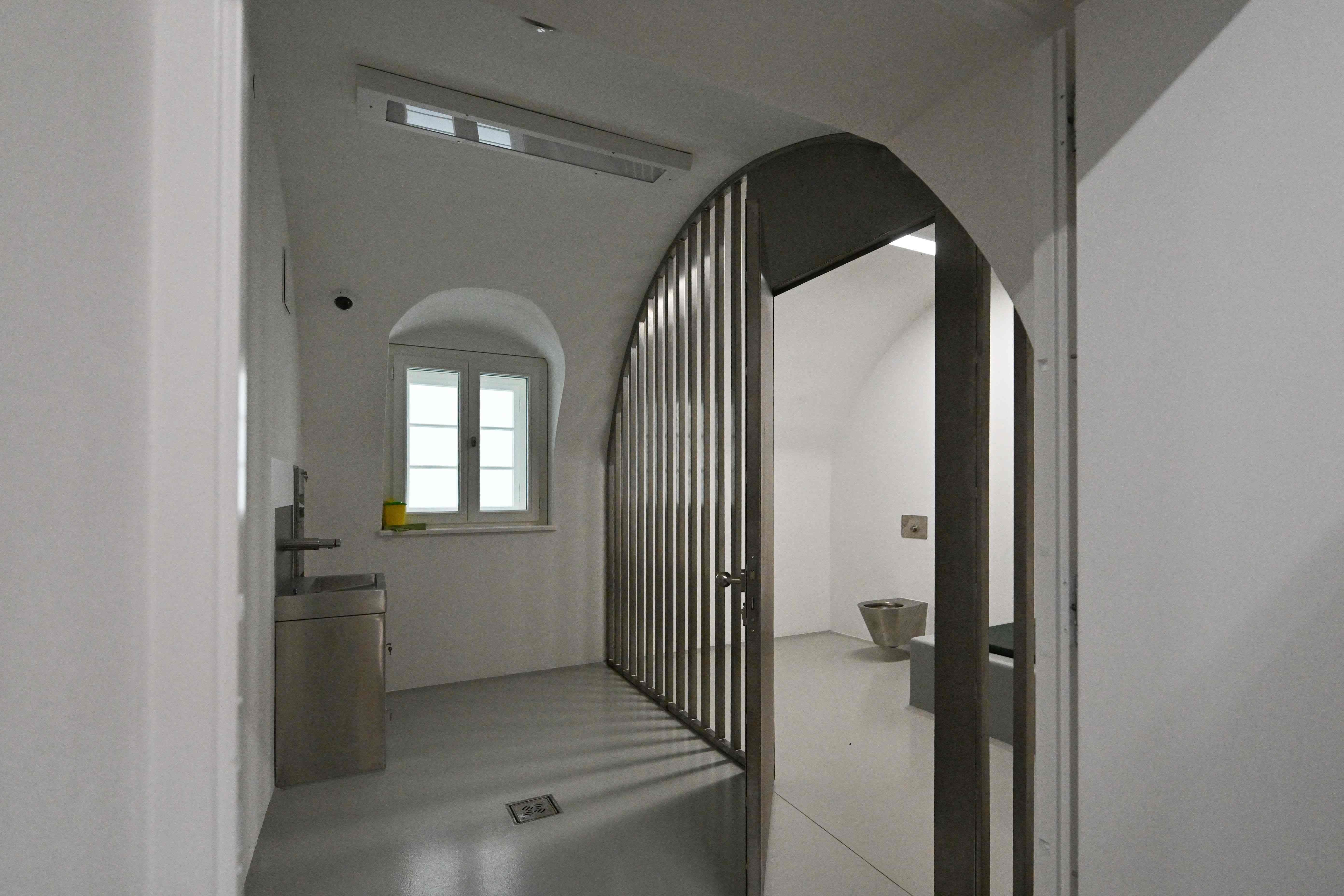 Blick in eine moderne Gefängniszelle mit Metallgittertür, Waschbecken und Toilette.