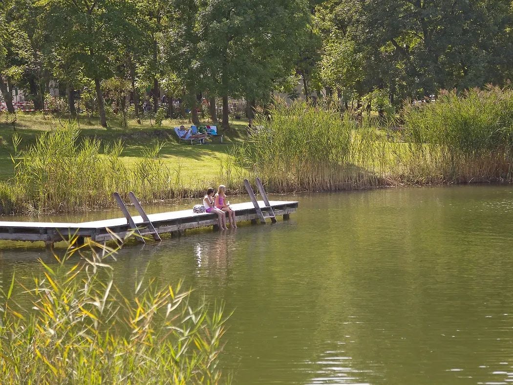 Zwei Mädchen sitzen auf einem Badesteg am Teich St. Margarethen, umgeben von Natur.