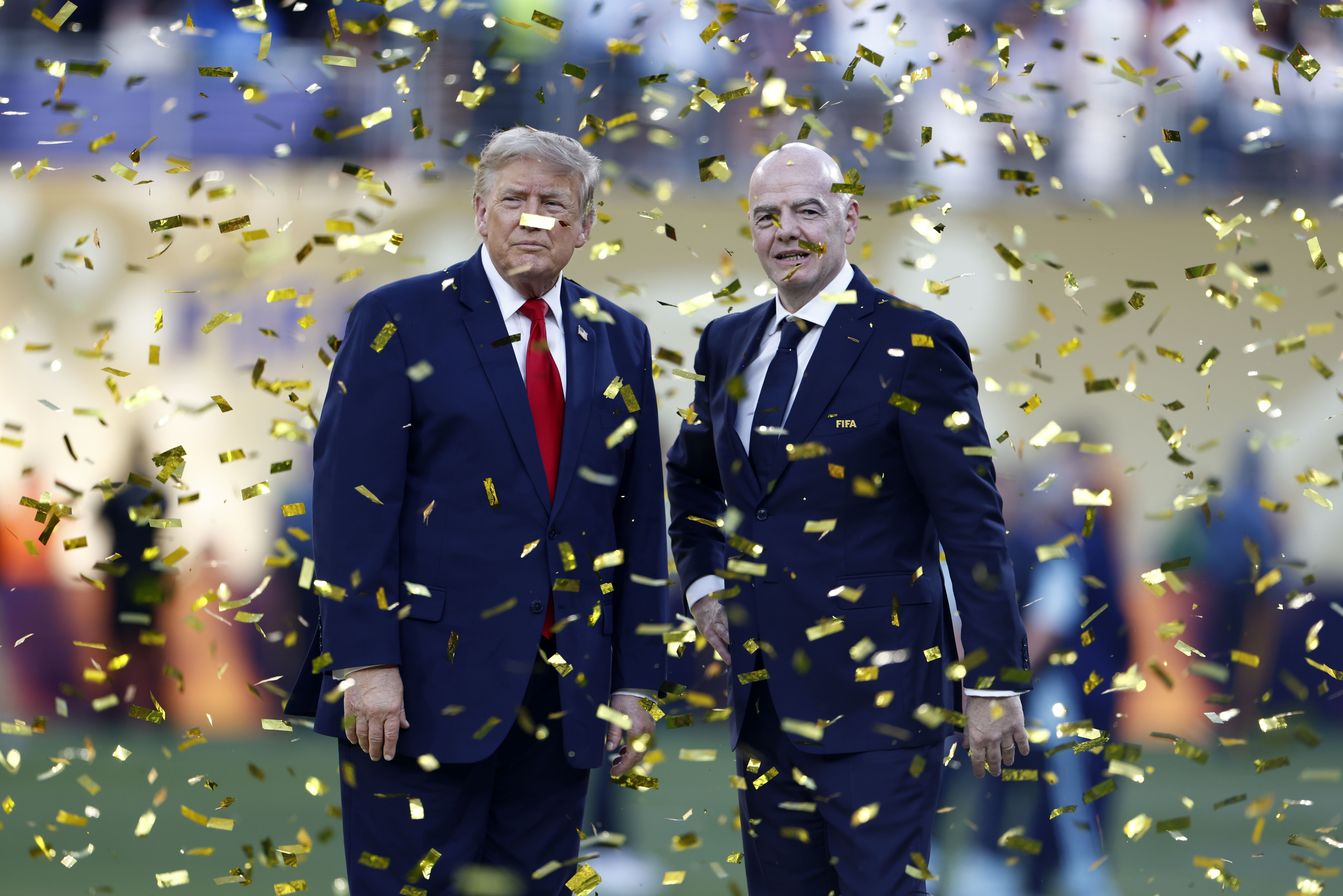 Zwei Männer im Anzug stehen unter goldenem Konfetti auf einem Fußballfeld.