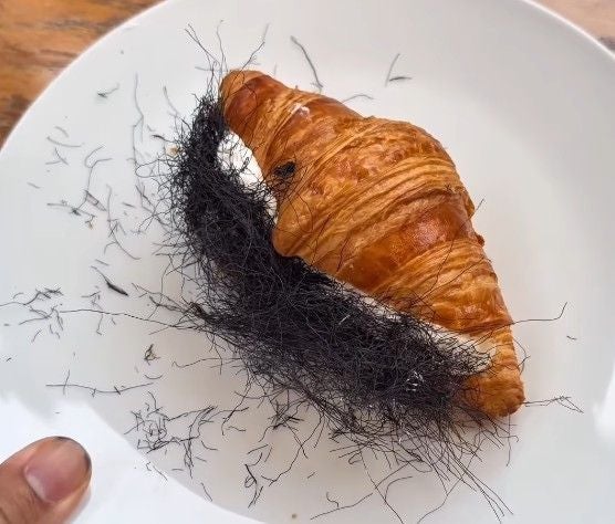 Ein Croissant mit dunklen Haaren auf einem weißen Teller.